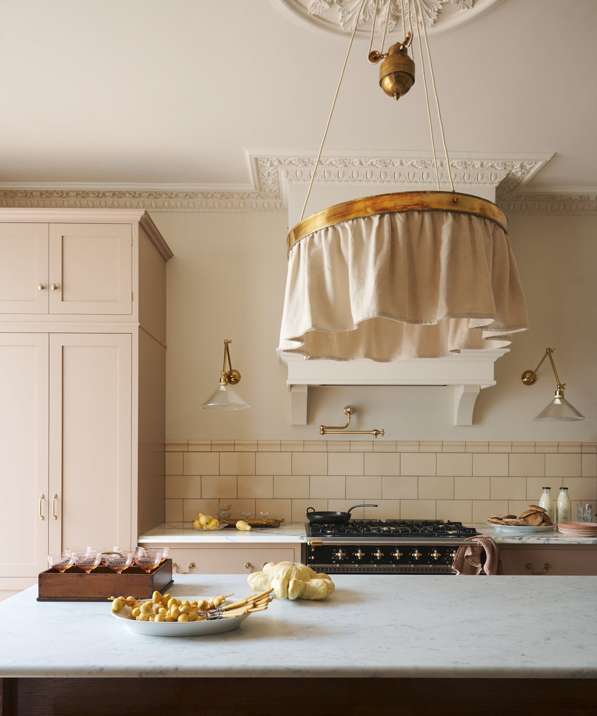 Cuisine crème de deVOL avec armoires pâles, comptoirs en marbre, accents en laiton et suspension en tissu au-dessus d'un grand îlot.