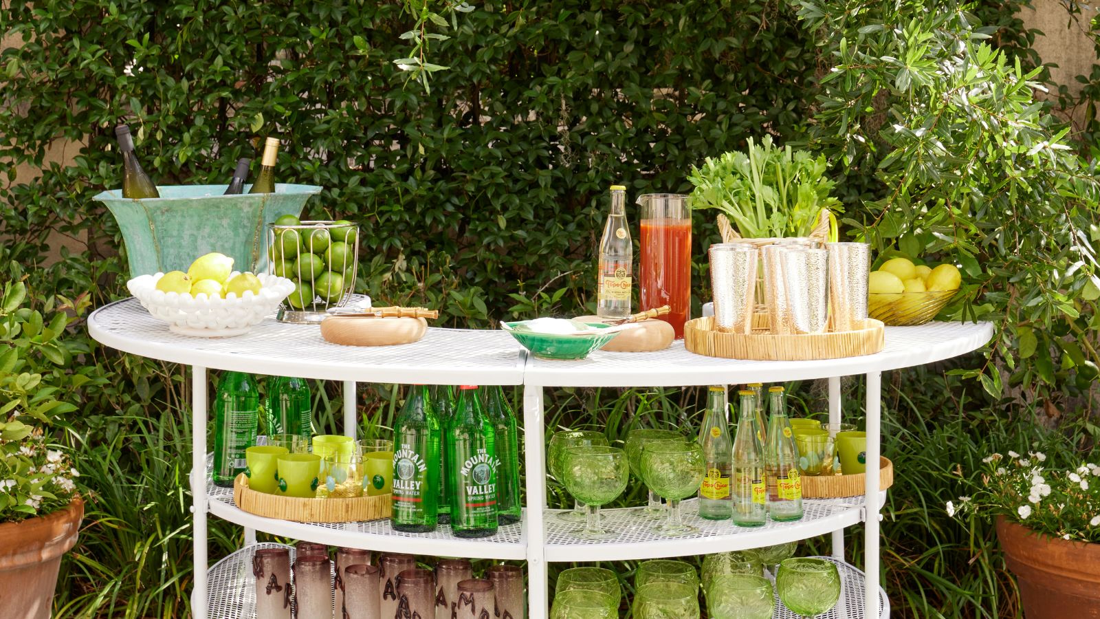 Station de boissons extérieure avec verrerie verte, plateaux en rotin et bols de fruits
