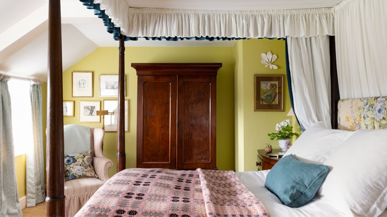 Chambre aux murs peints en vert citron, un lit à baldaquin en acajou avec un baldaquin, une tête de lit fleurie et une couverture galloise rose, et une grande armoire en acajou à côté d'un fauteuil rose pâle.