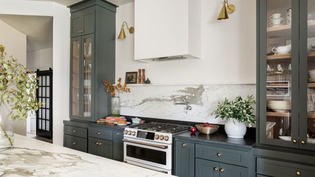 Modern farmhouse style kitchen with marble backsplash, dark green cabinets painted in Sherwin-Williams Pewter Green, and glass-fronted cabinets filled with tableware.