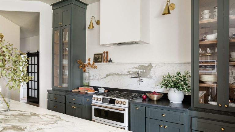 Modern farmhouse style kitchen with marble backsplash, dark green cabinets painted in Sherwin-Williams Pewter Green, and glass-fronted cabinets filled with tableware.