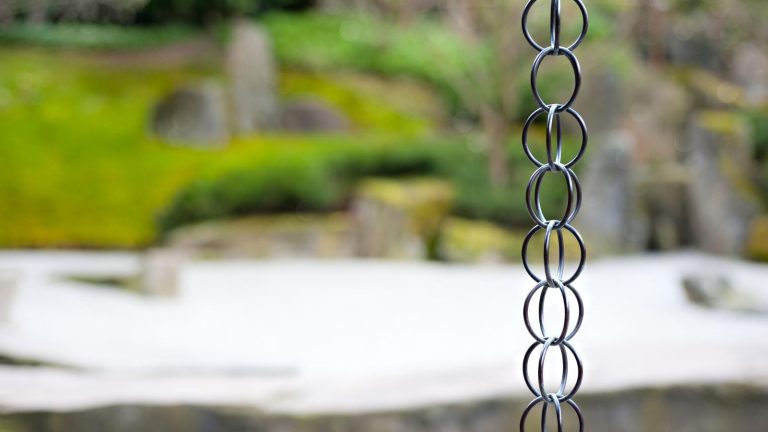 A rain chain in focus in front of a blurry garden