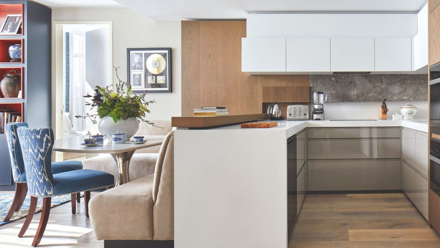 5 appareils électroménagers que vous devriez toujours débrancher avant de partir en vacances pour éviter de gaspiller de l’énergie et de risquer des dommages A bright kitchen with white cabinets and wooden flooring. To the left is a comfortable seating/ dinign area with a beige sofa chair, table, and blue patterned seats with wooden legs. To the far left is a blue bookshelf.
