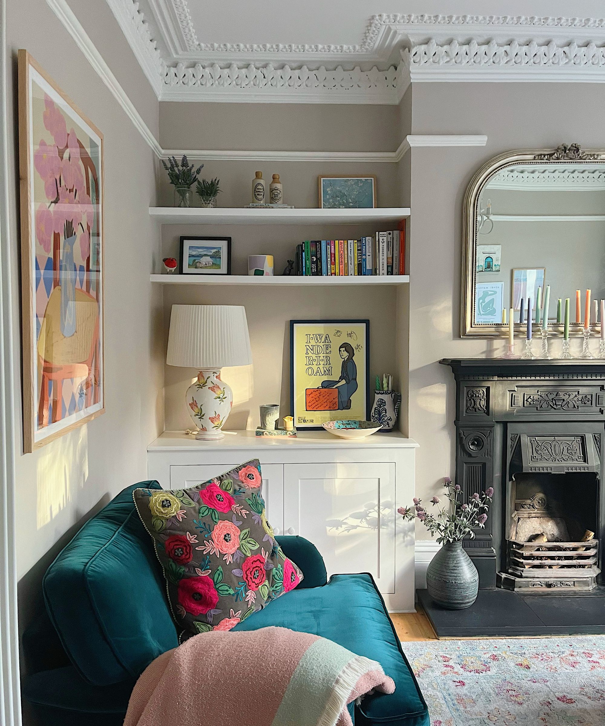 Salon avec moulures, Farrow &amp; Ball's Elephant Breath sur les murs, une alcôve intégrée avec des étagères et des œuvres d'art, un canapé en velours bleu, un tapis persan et une grande cheminée noire victorienne.