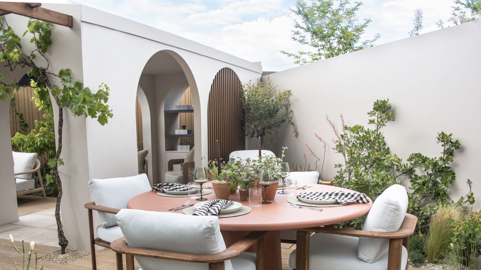 Cet astucieux monsieur de terrasse vous rafraîchit instantanément en cas de canicule – pour que vous puissiez réellement profiter de votre jardin toute la journée A round outdoor dining table with four chairs on a modern patio with white walls and archways