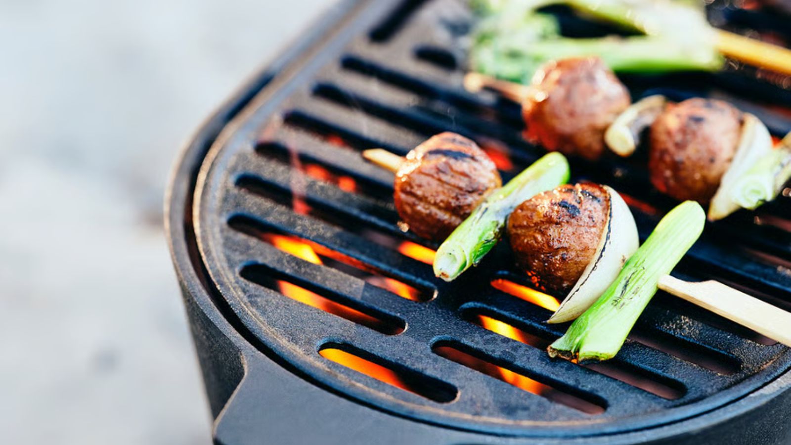 Un gros plan de boulettes de viande et de légumes sur des bâtons de bois sur un barbecue en fonte  