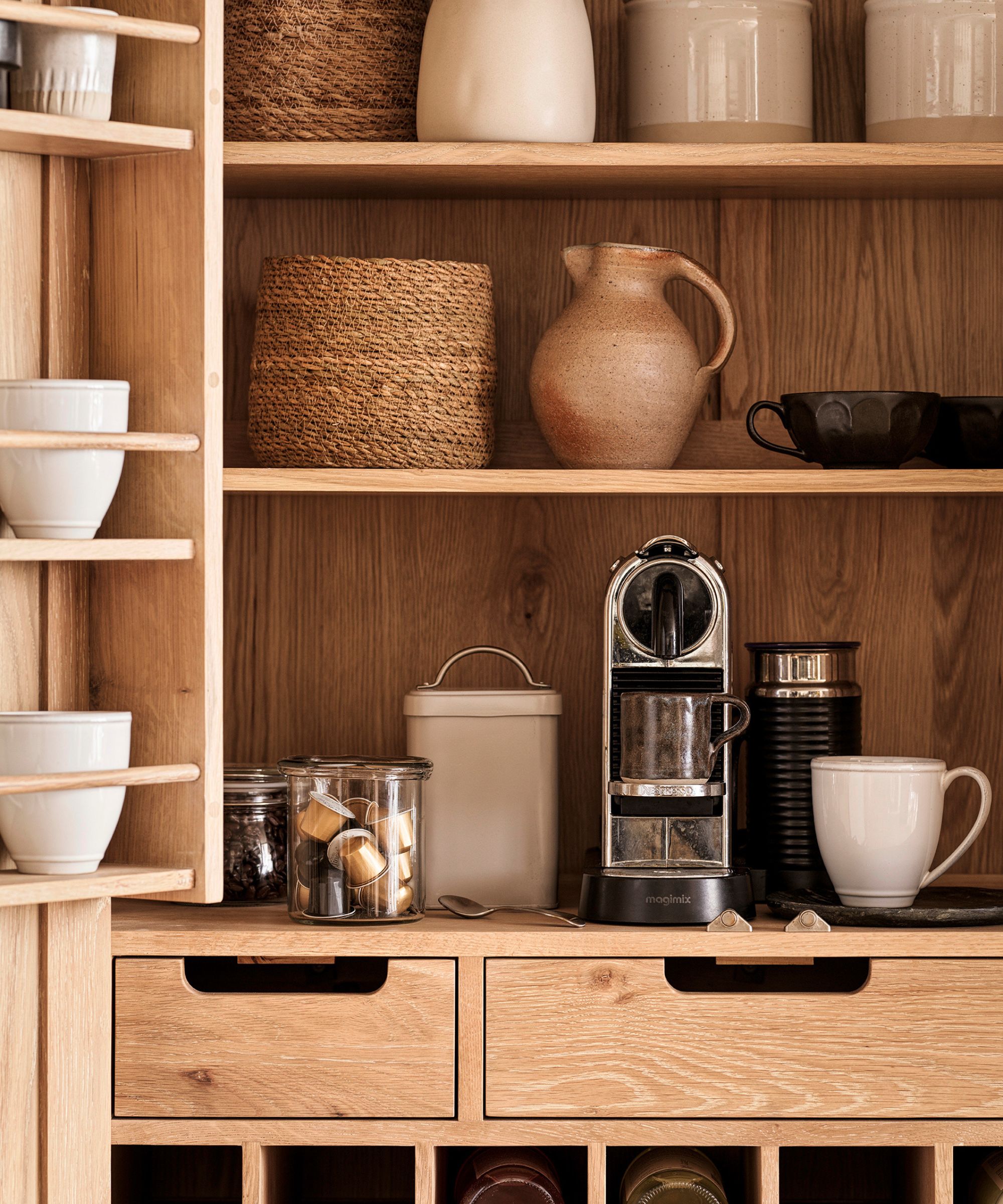 L'intérieur d'un garde-manger en bois avec étagères. Une cafetière sur l'étagère du bas, des casseroles et des paniers sur les étagères du dessus.