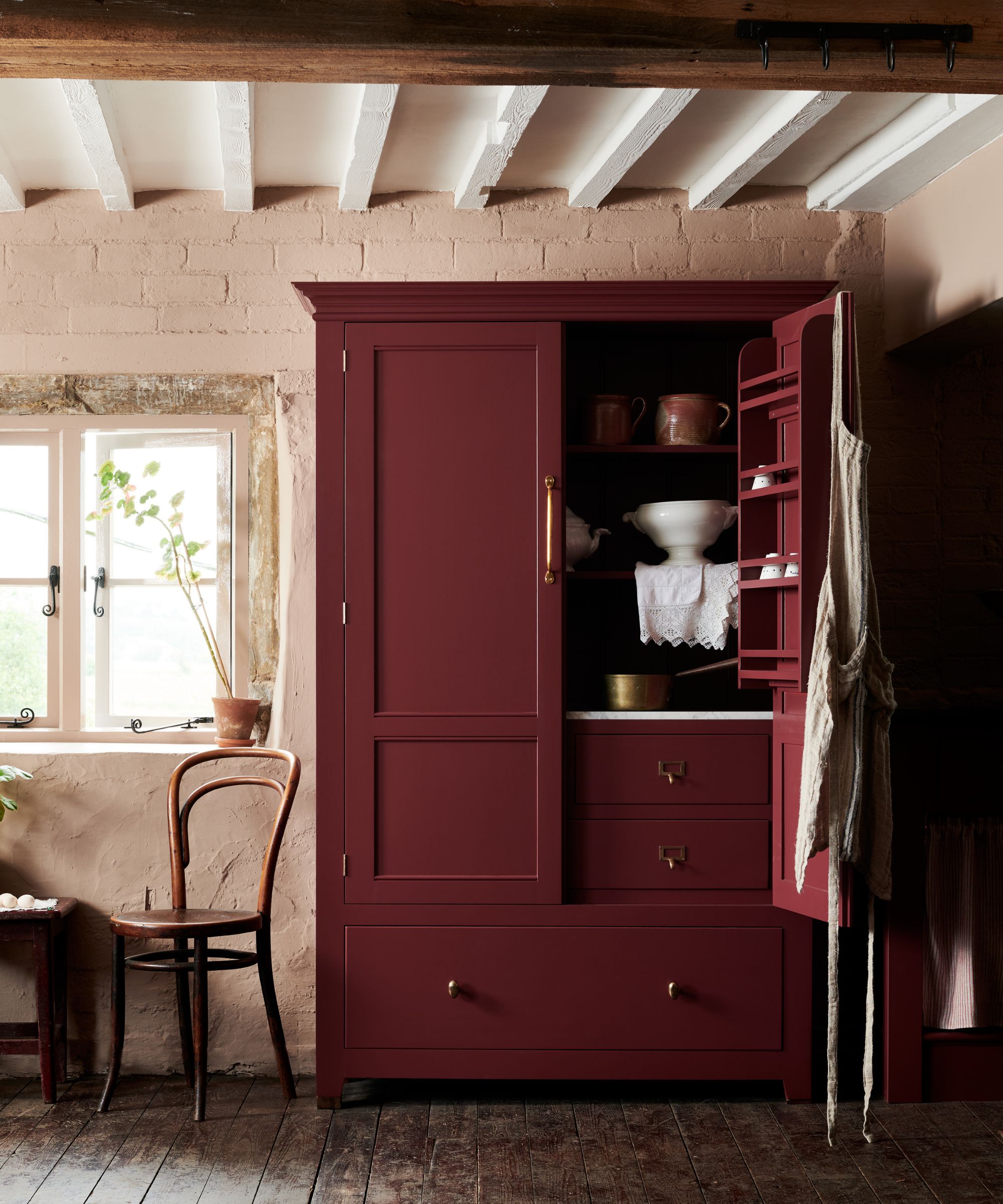Garde-manger rouge bordeaux dans le rouge réfectoire de deVOL, posé contre des murs en plâtre rustique, des poutres en bois apparentes et un parquet en bois vieilli.