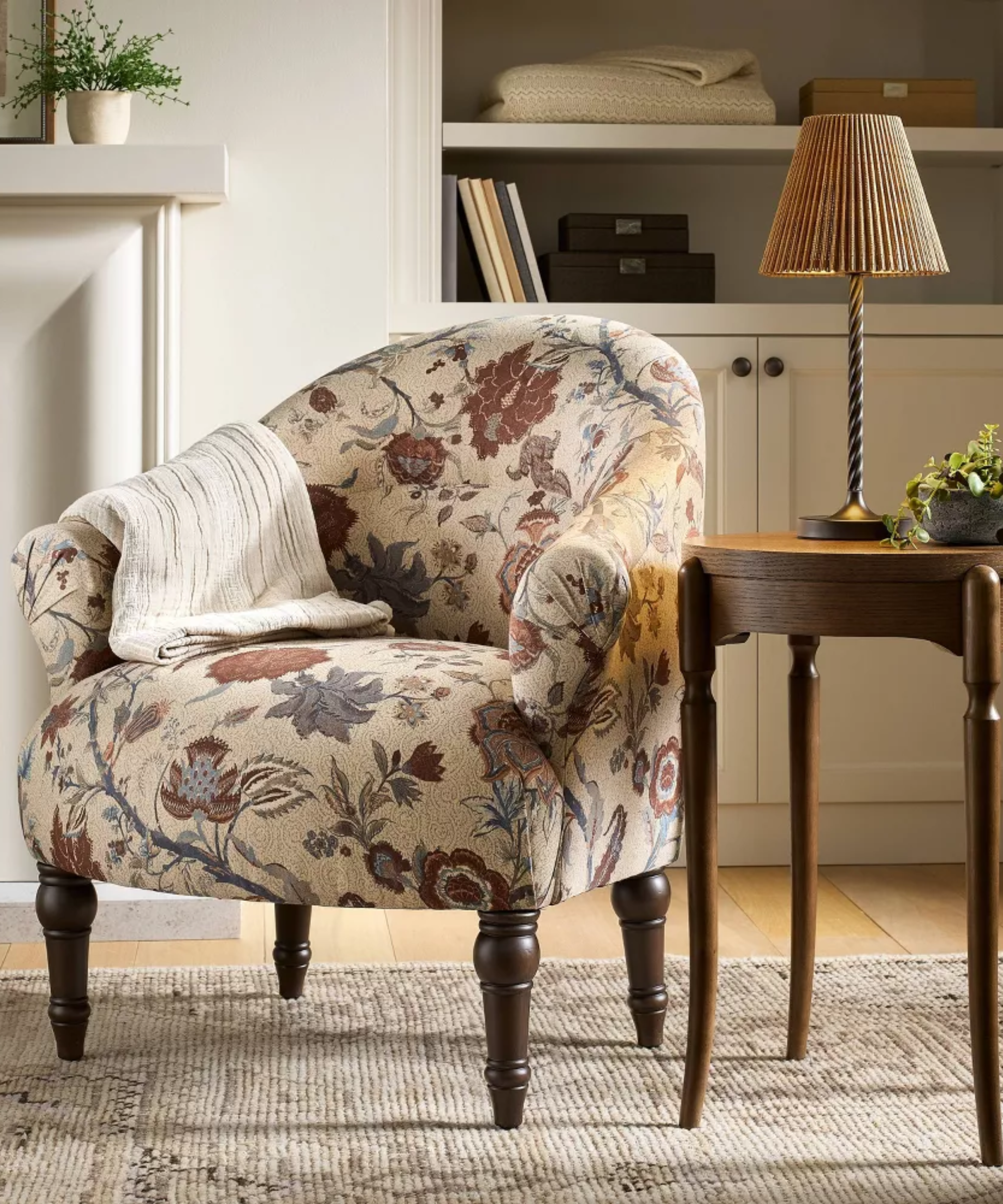 une chaise fleurie avec une couverture drapée sur le côté, une table d'appoint et une lampe portative