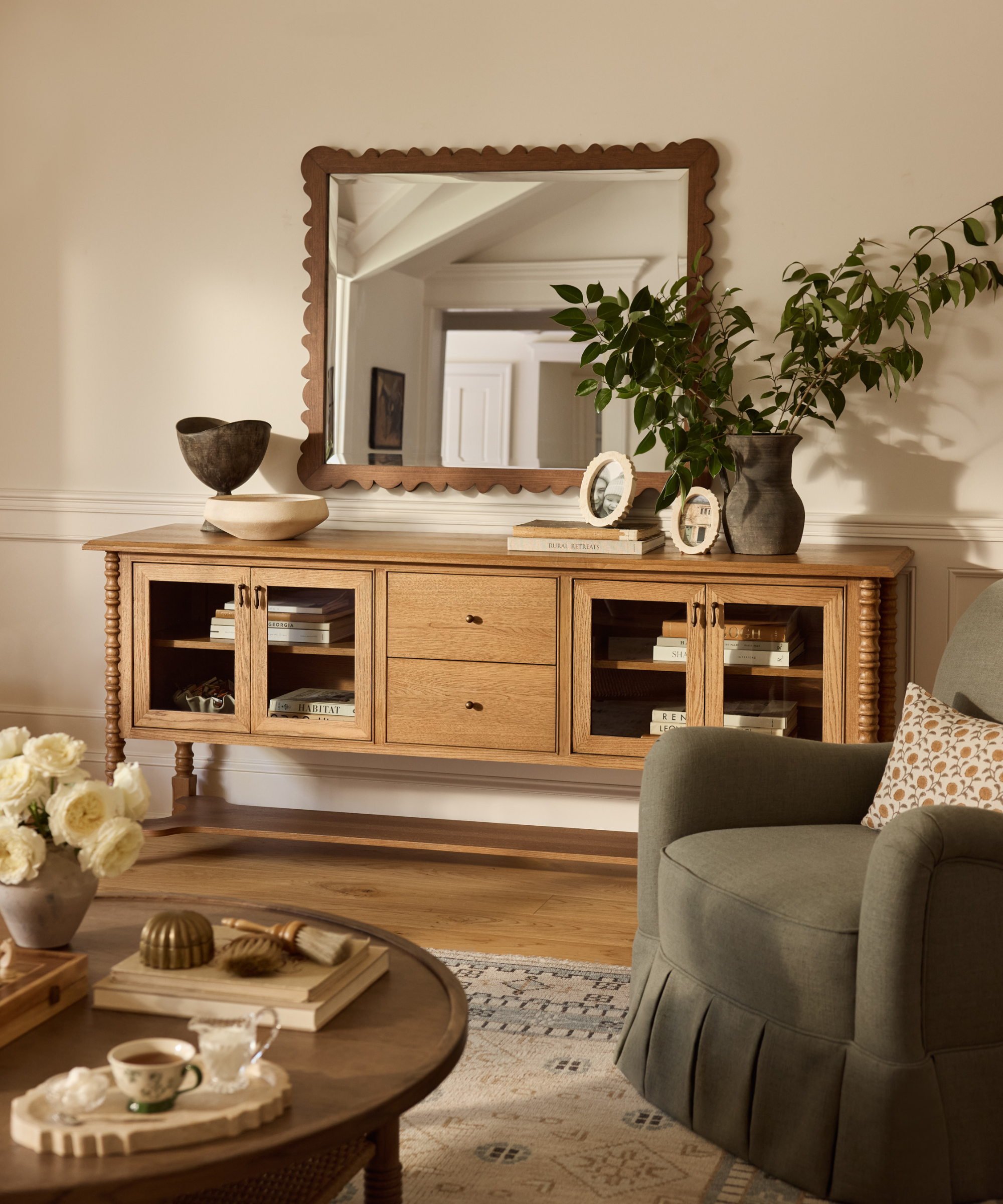 un salon avec une grande crédence en bois, un miroir décoratif, une chaise d'appoint verte et une table basse au premier plan