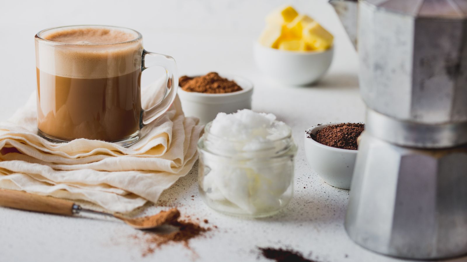 Comment faire du café pare-balles : de l'huile de coco, du beurre, de la cannelle et une cafetière moka autour d'une tasse de café pare-balles