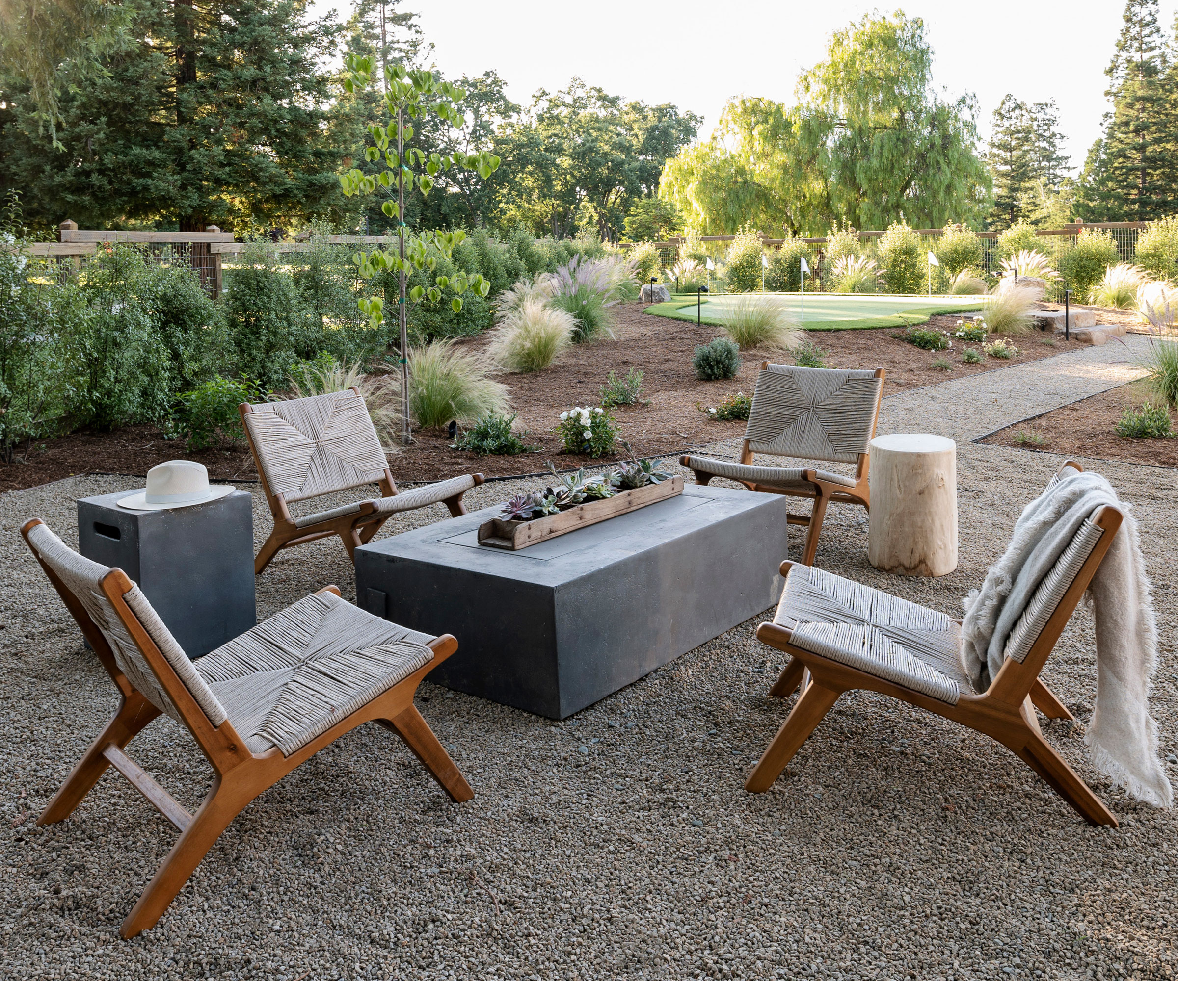 conception de cour arrière paysagée avec gravier, table de feu, chaises de jardin, chemin et plantation