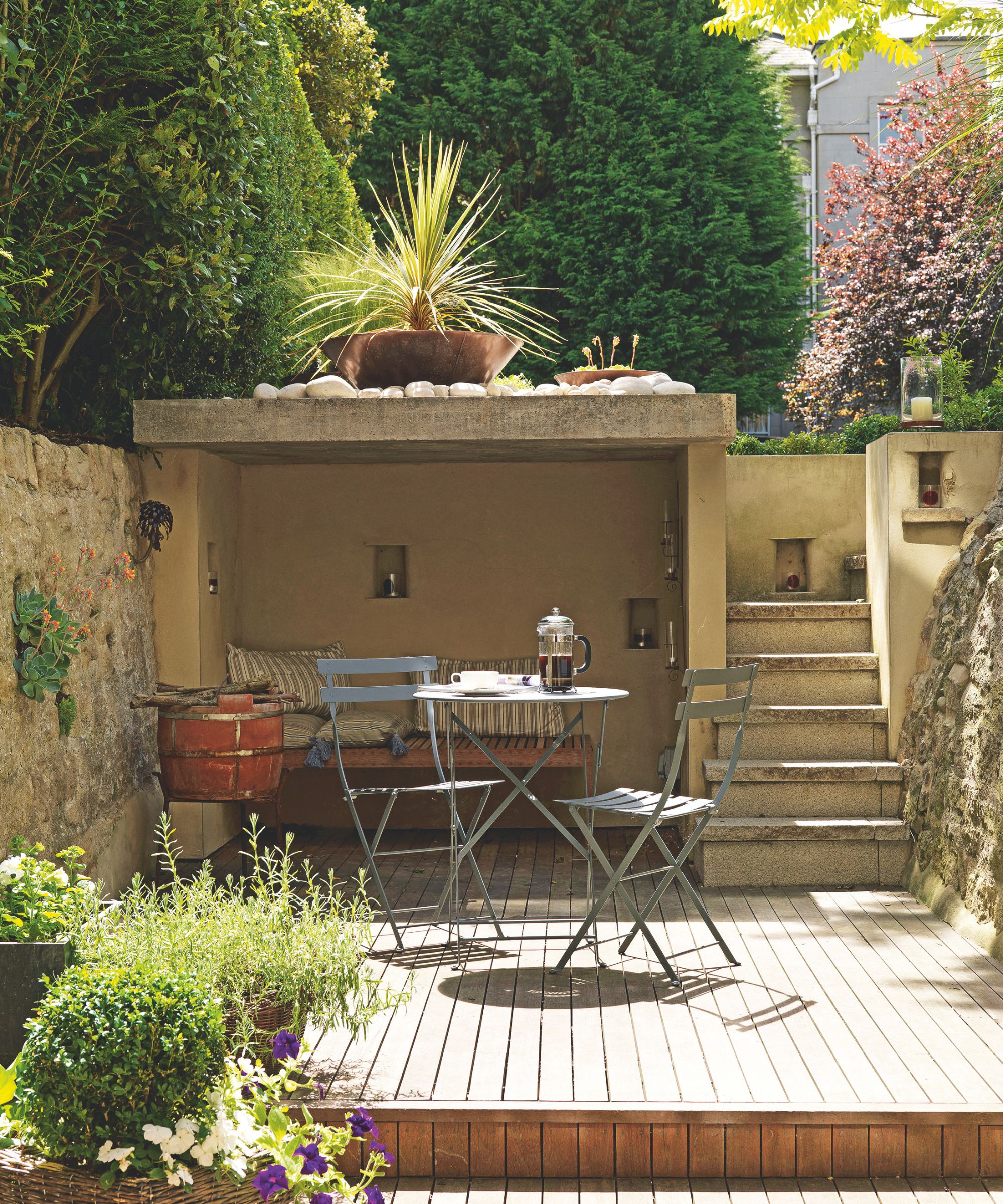 Petite terrasse avec escalier menant au jardin, un niveau avec parquet en bois, ensemble bistro en métal et alcôve avec banquette intégrée et coussins rayés.