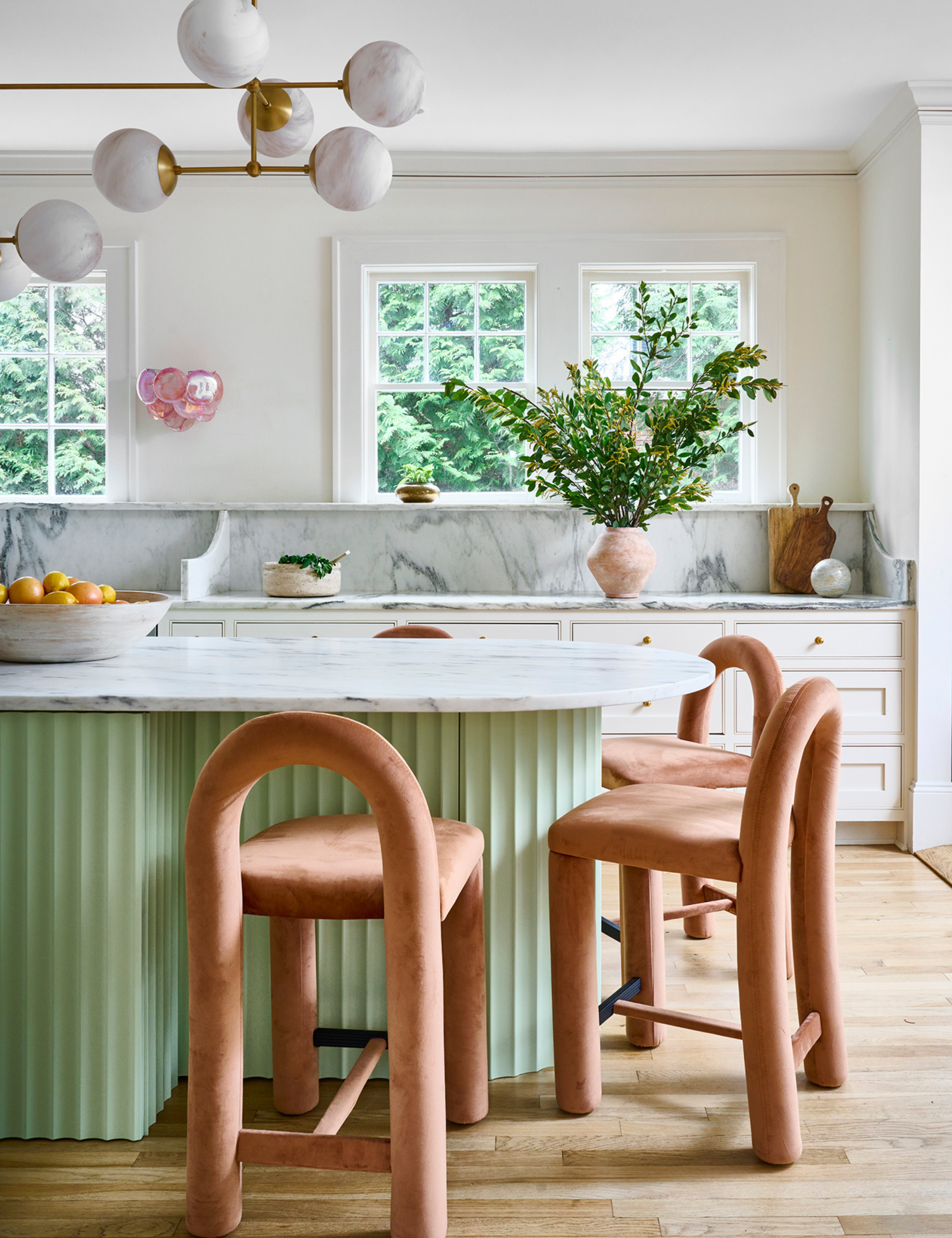 Coin cuisine chaleureux avec un îlot vert menthe entouré de chaises de salle à manger contemporaines couleur pêche.