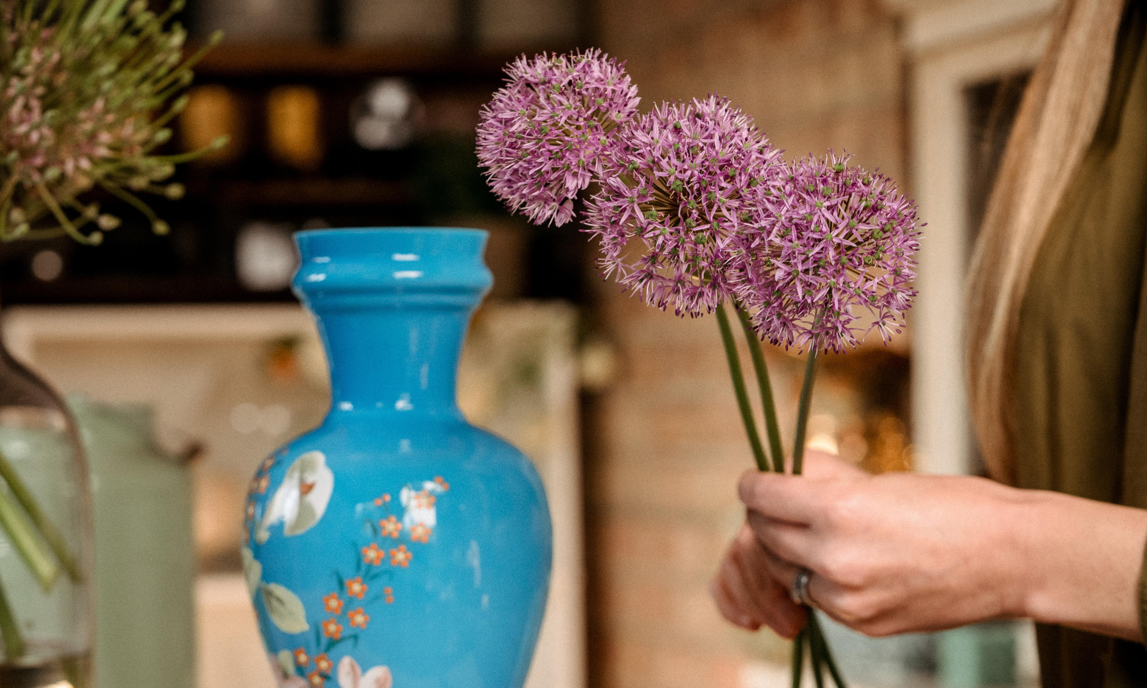 Mains tenant trois alliums globe à côté d'un vase bleu vintage
