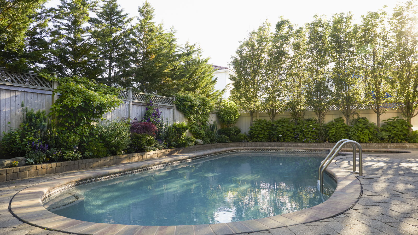 Une piscine dans la cour entourée de parterres de fleurs et d'arbres