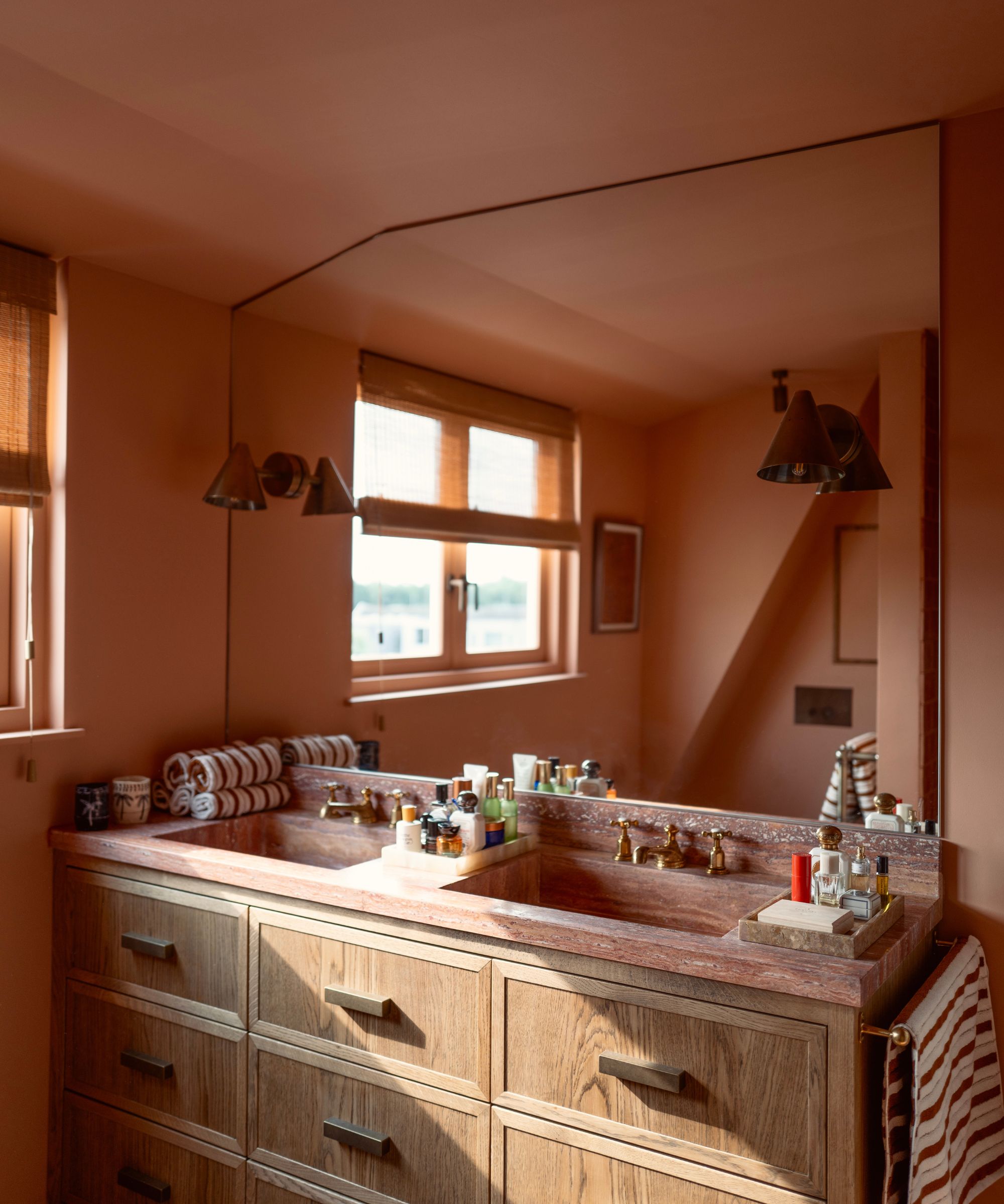 Salle de bain avec Naperon de Farrow &amp; Des murs peints en boule, un meuble double vasque en bois avec un dessus en marbre rouge et un grand miroir avec deux appliques en laiton de chaque côté.