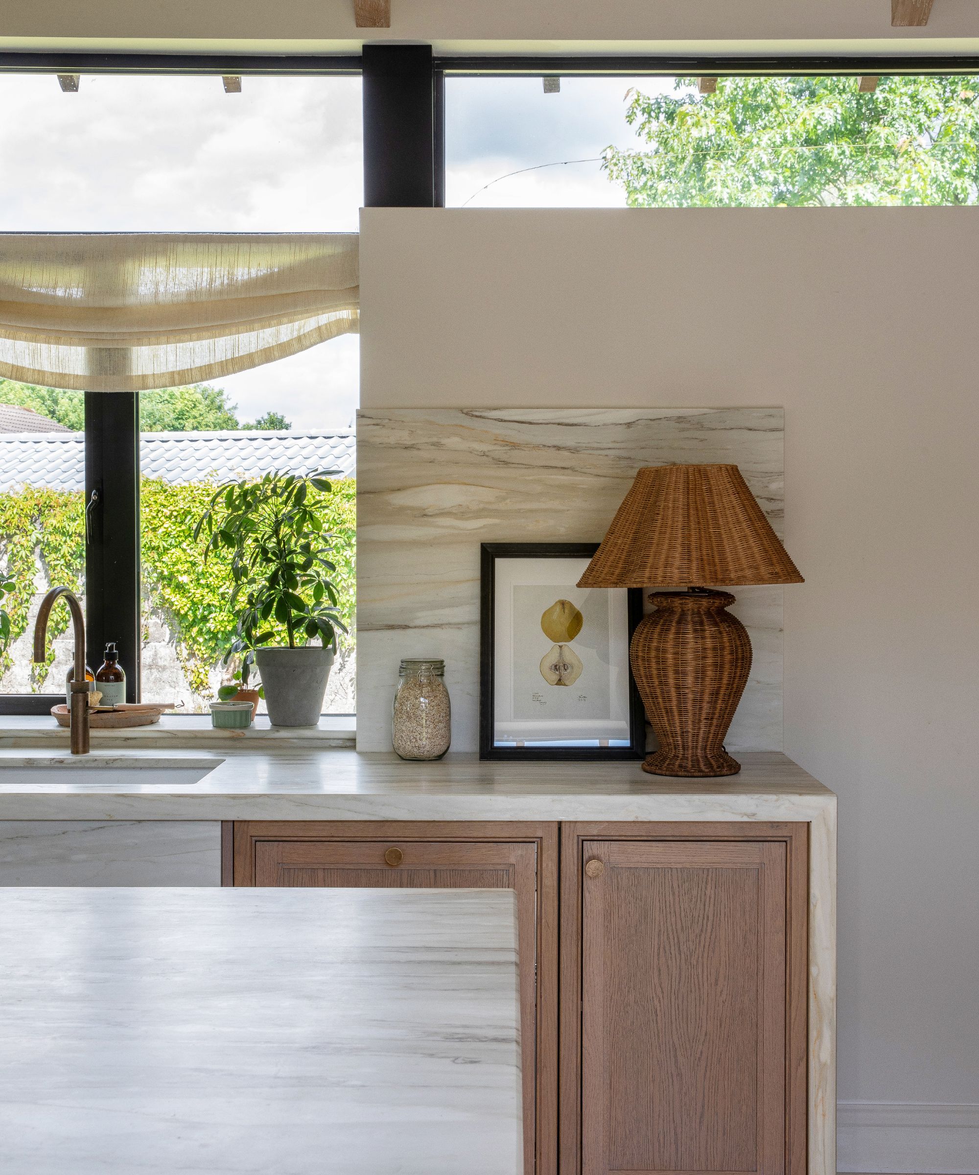 Le coin d'une cuisine en bois avec des murs blancs, des comptoirs en marbre et une décoration collectionnée, comprenant une lampe en rotin et des œuvres d'art encadrées
