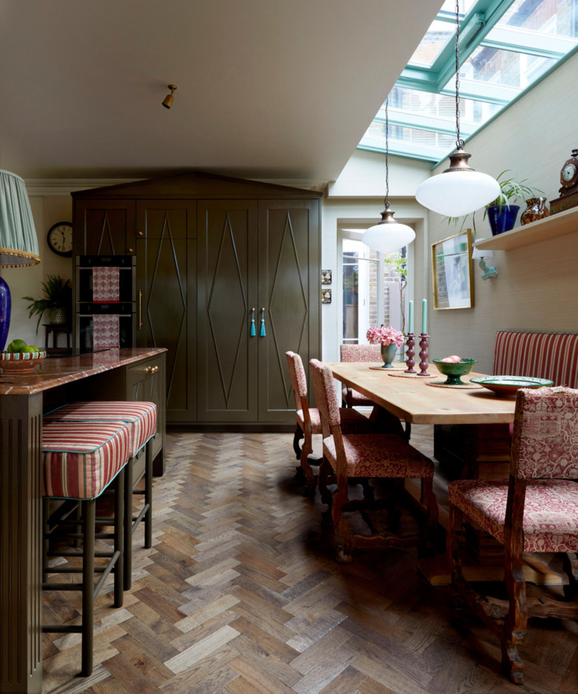 Une grande cuisine avec parquet et armoires vert olive foncé recouvertes d'accessoires rouge foncé