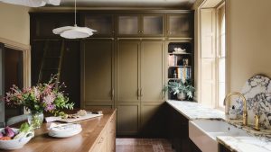 Pourquoi les cuisines « discrètement dramatiques » définissent les plus grandes tendances de design de 2026 – et comment recréer ce look élégant A kitchen with olive green cabinets, marble countertops, and a wooden island