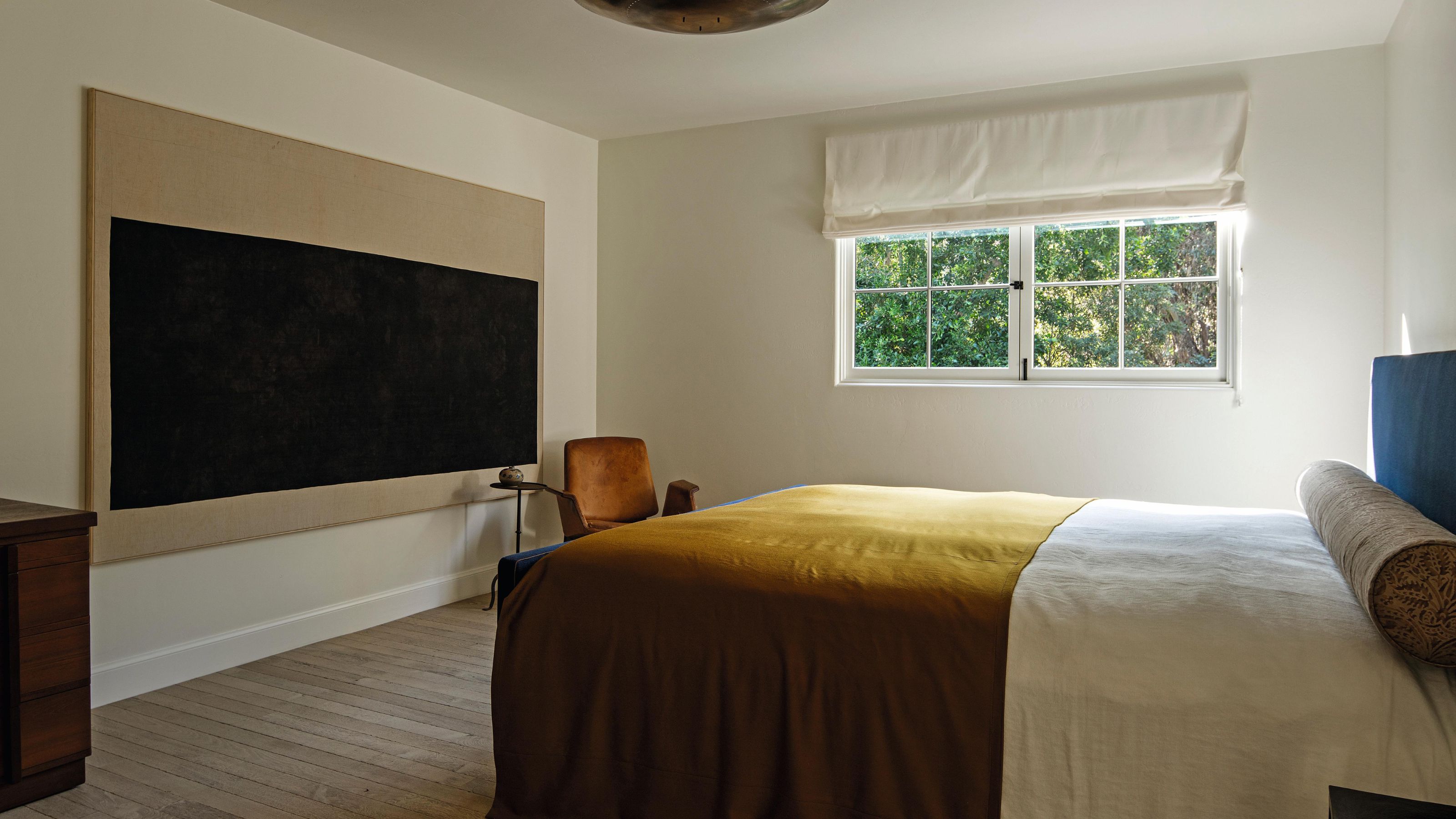 une grande chambre neutre avec de l'art abstrait et une tête de lit bleue avec une couverture moutarde sur le lit