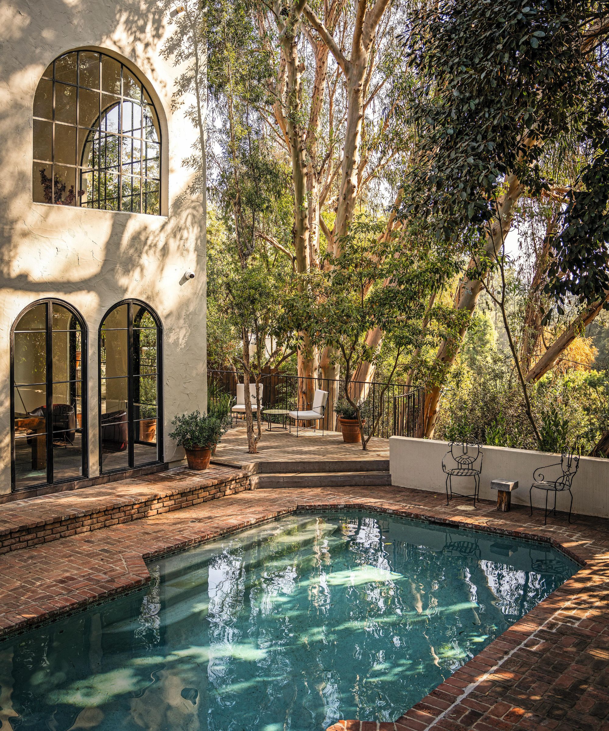 une maison bordée d'arbres à Los Angeles avec des fenêtres cintrées et une piscine pavée en brique et une terrasse