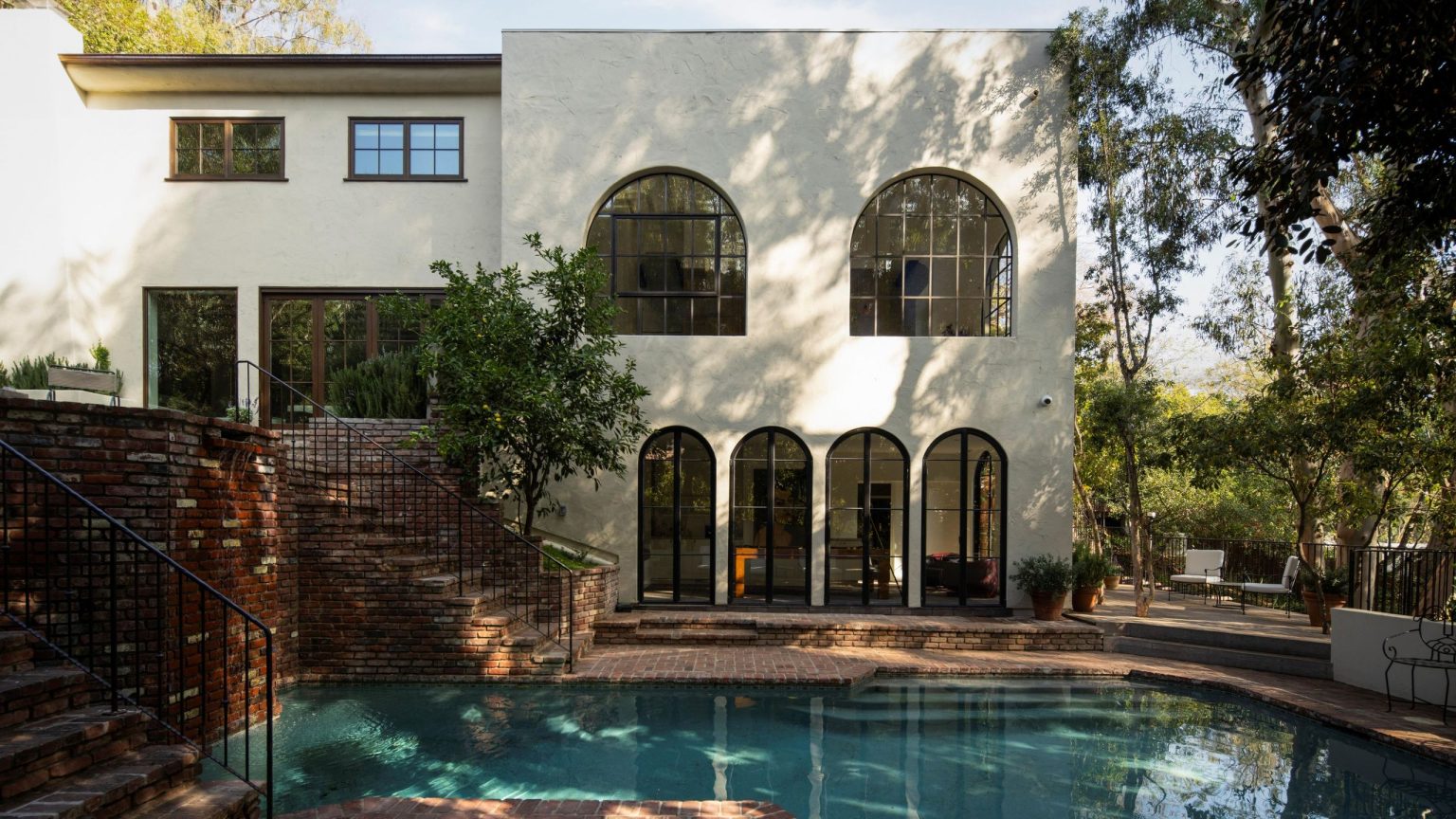 La décision la plus audacieuse dans cette maison californienne a laissé tant de choses en suspens – « La simplicité lui permet de chanter » a large LA rendered home with brick patio and stairs with a pool and trees overhead
