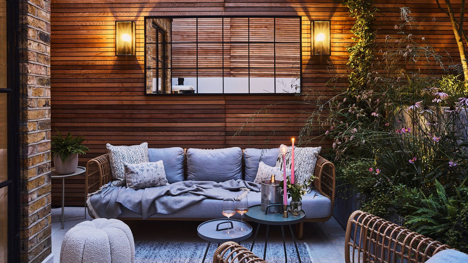 Terrasse extérieure revêtue de bois avec éclairage du soir, canapé confortable et tables d'appoint avec bougies et verres de vin