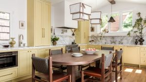 A butter yellow kitchen with a marble countersplash and a wooden kitchen table instead of an island