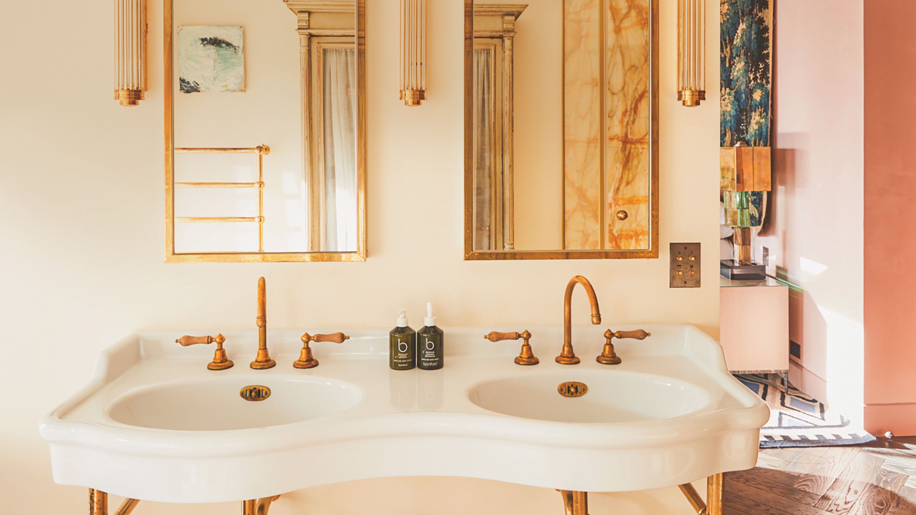 Vanité double en porcelaine blanche avec robinets en laiton vintage et miroirs aux cadres dorés contre des murs crème