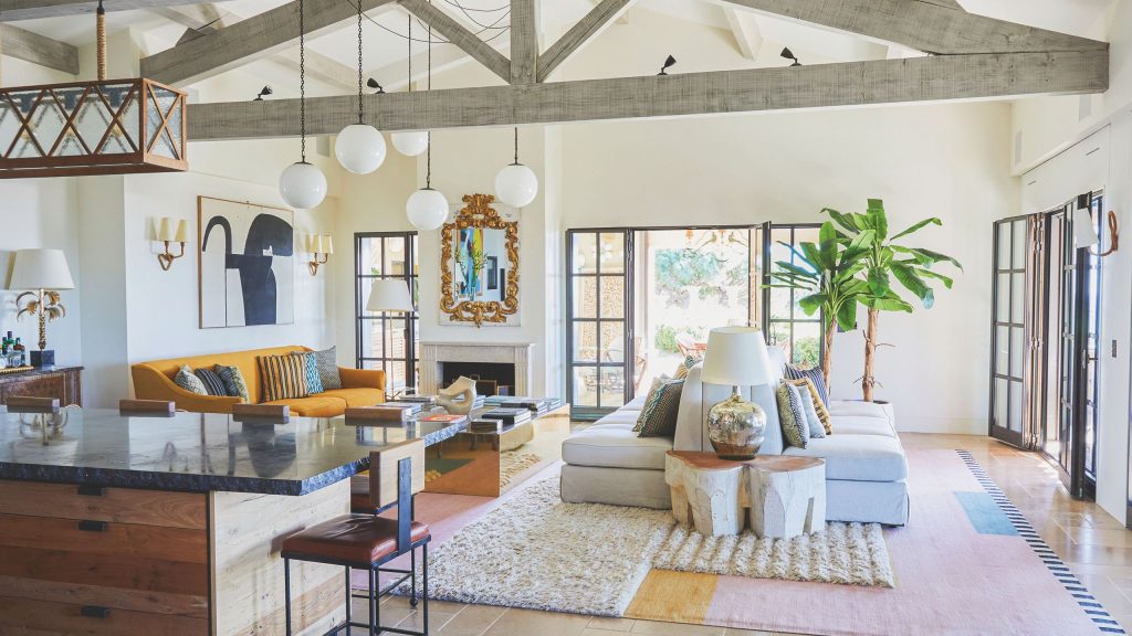 Bright open-plan living room with exposed beams, a gray sofa, an orange sofa, and kitchen island