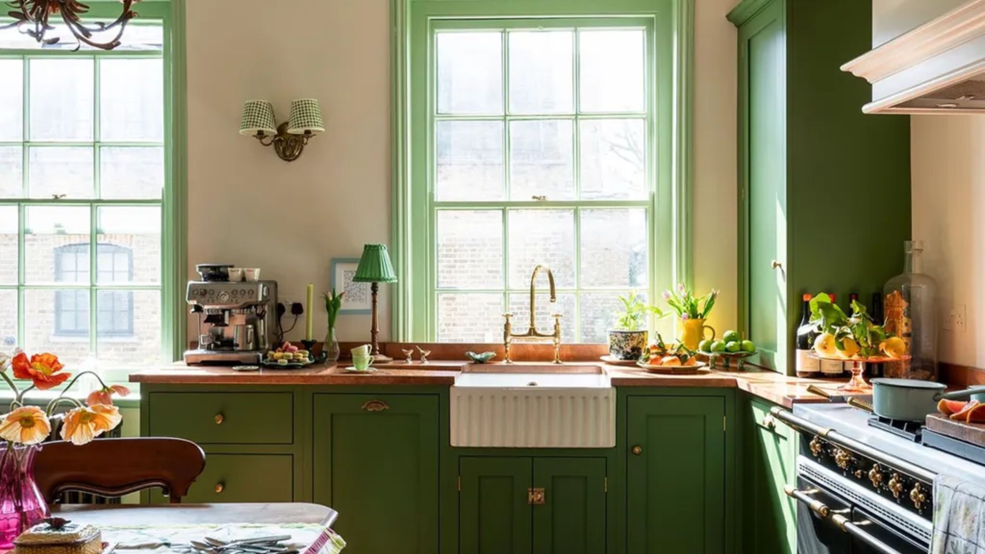 Une petite cuisine avec des armoires vertes, des comptoirs en cuivre, une cuisinière et un ensemble table et chaises vintage