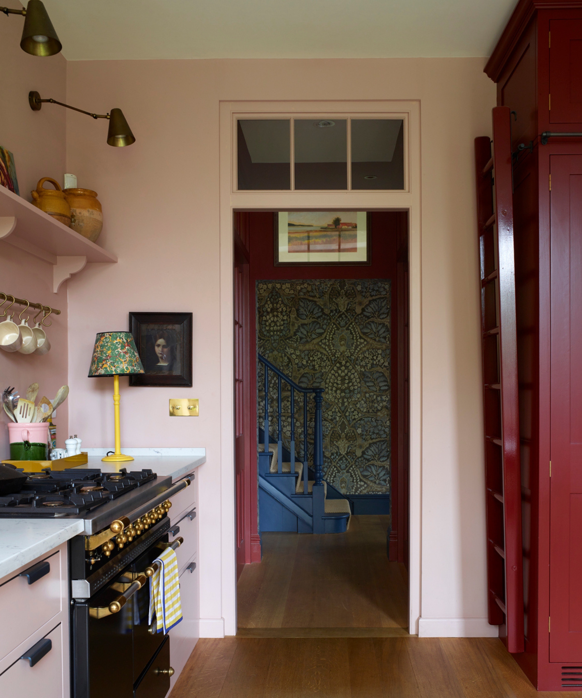 Une cuisine rose avec des appliques murales en laiton et une contre-lampe jaune vif avec un abat-jour à motifs verts