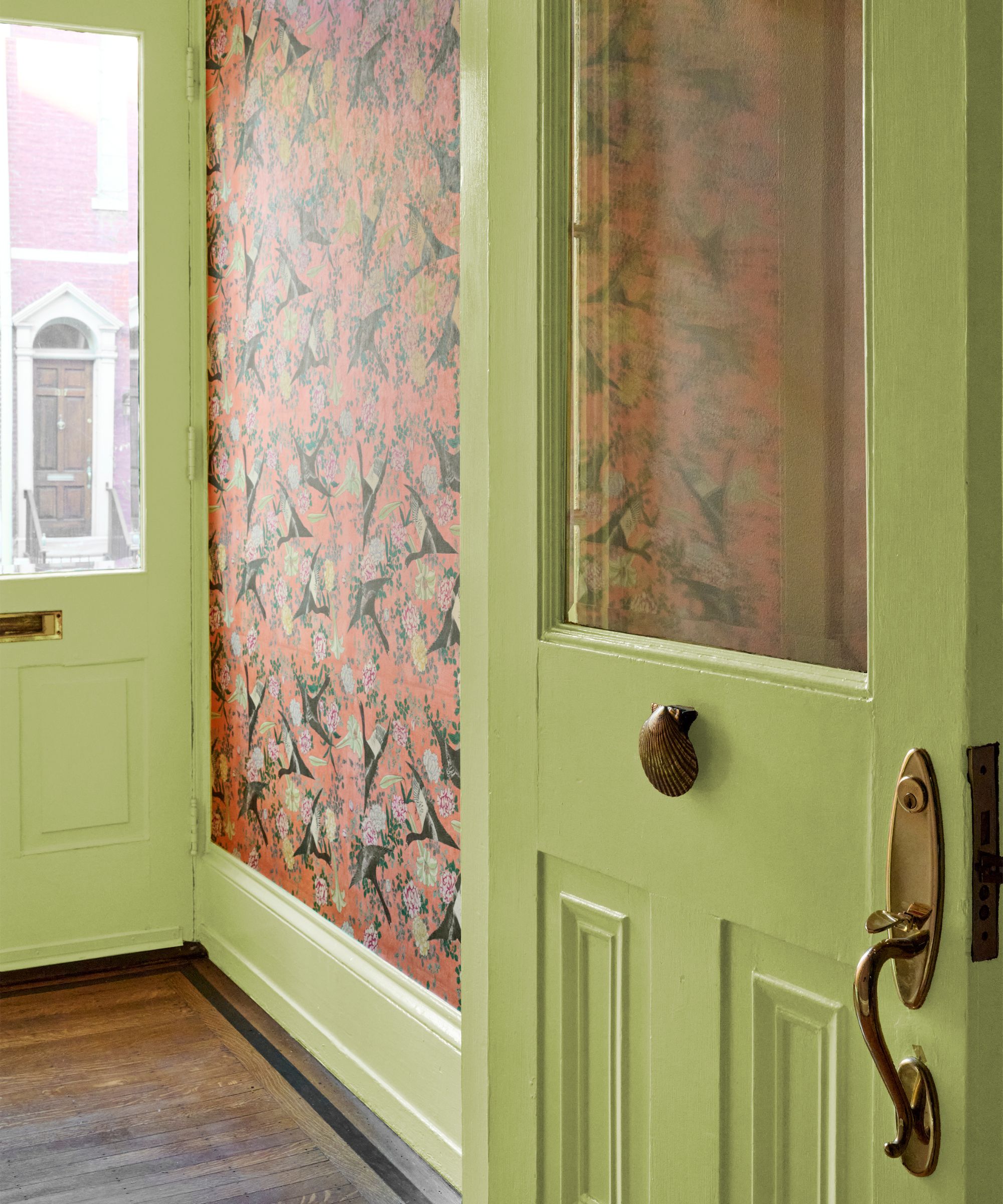 Entrée avec portes peintes en vert chartreuse, quincaillerie en laiton et papier peint corail vibrant avec un motif d'oiseau.