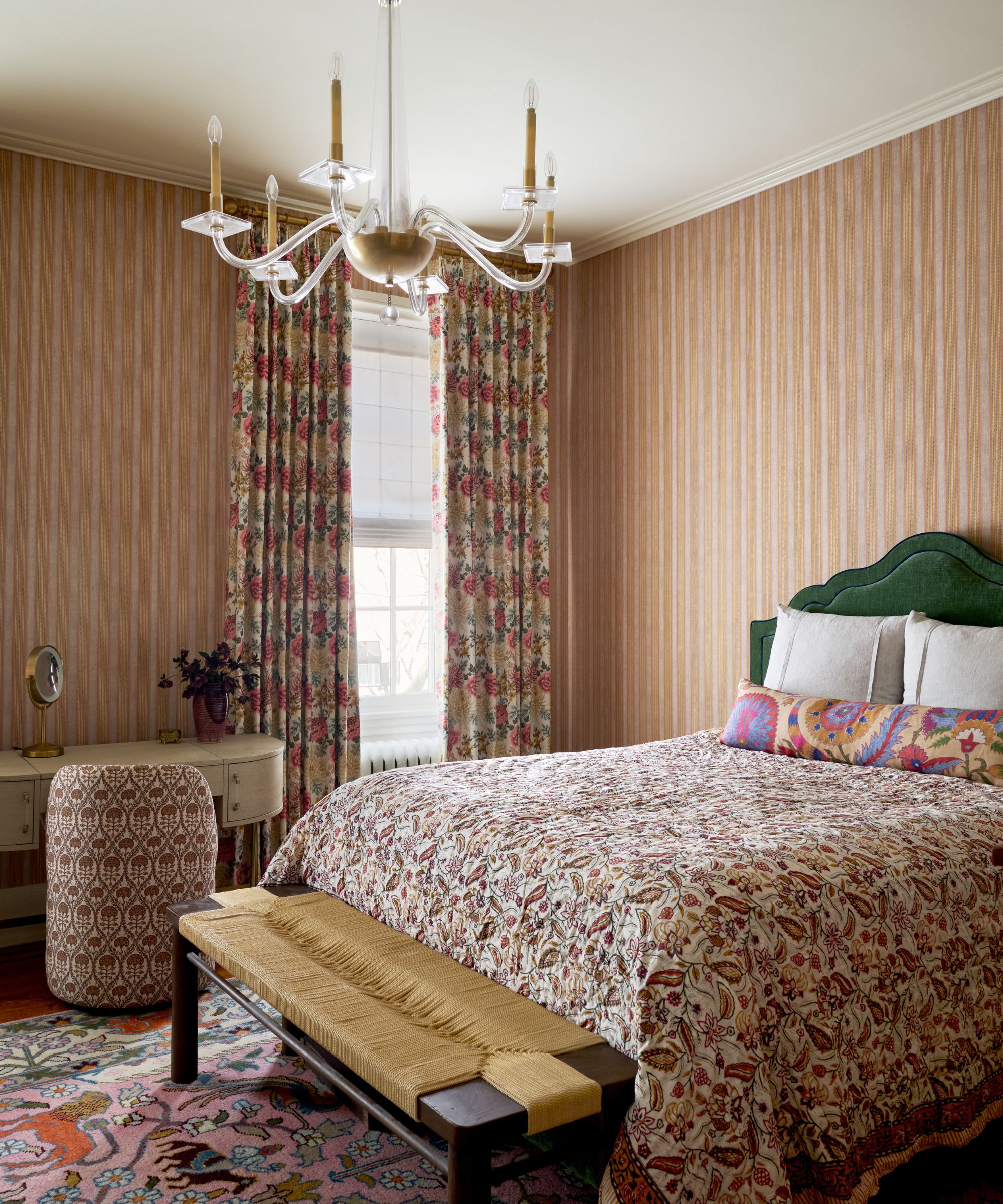 Chambre maximaliste avec papier peint à rayures roses, tête de lit en velours vert, couette à motif cachemire colorée et lustre en verre.