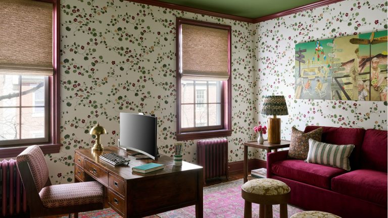 Une collection d’art précieuse a inspiré chaque pièce de cette maison historique originale Home office with floral wallpaper, green ceiling, vintage wooden desk, burgundy velvet sofa, and a vibrant pink rug.
