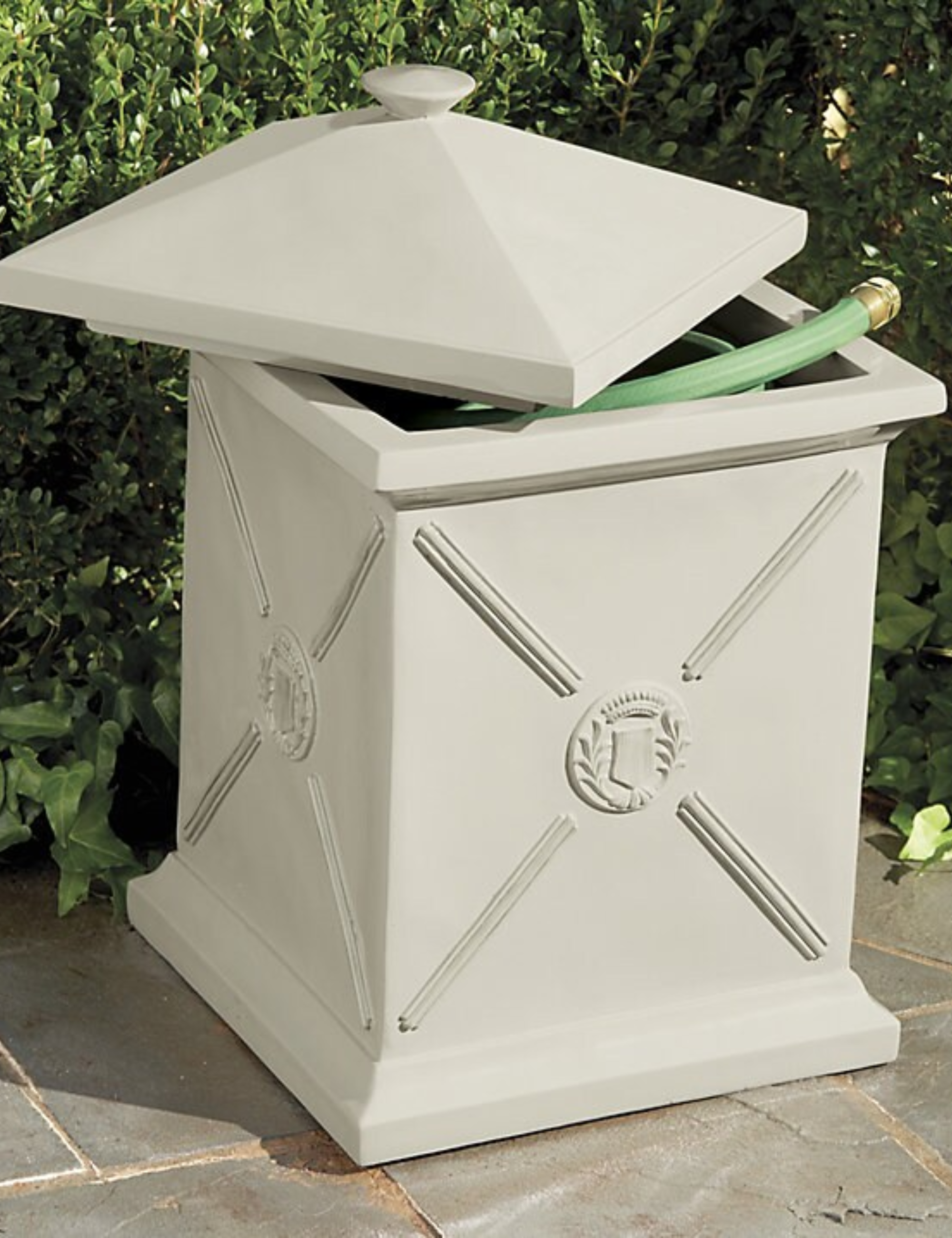 Pot d'arrosage de style antique situé au sommet d'un patio en pierre avec haie