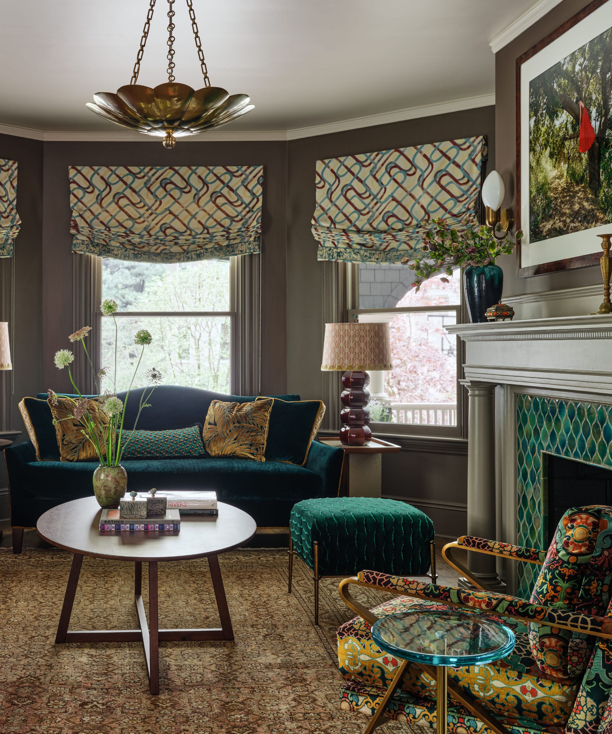 Salon éclectique avec un canapé en velours bleu sarcelle, un fauteuil à motifs et une cheminée aux détails carrelés verts.