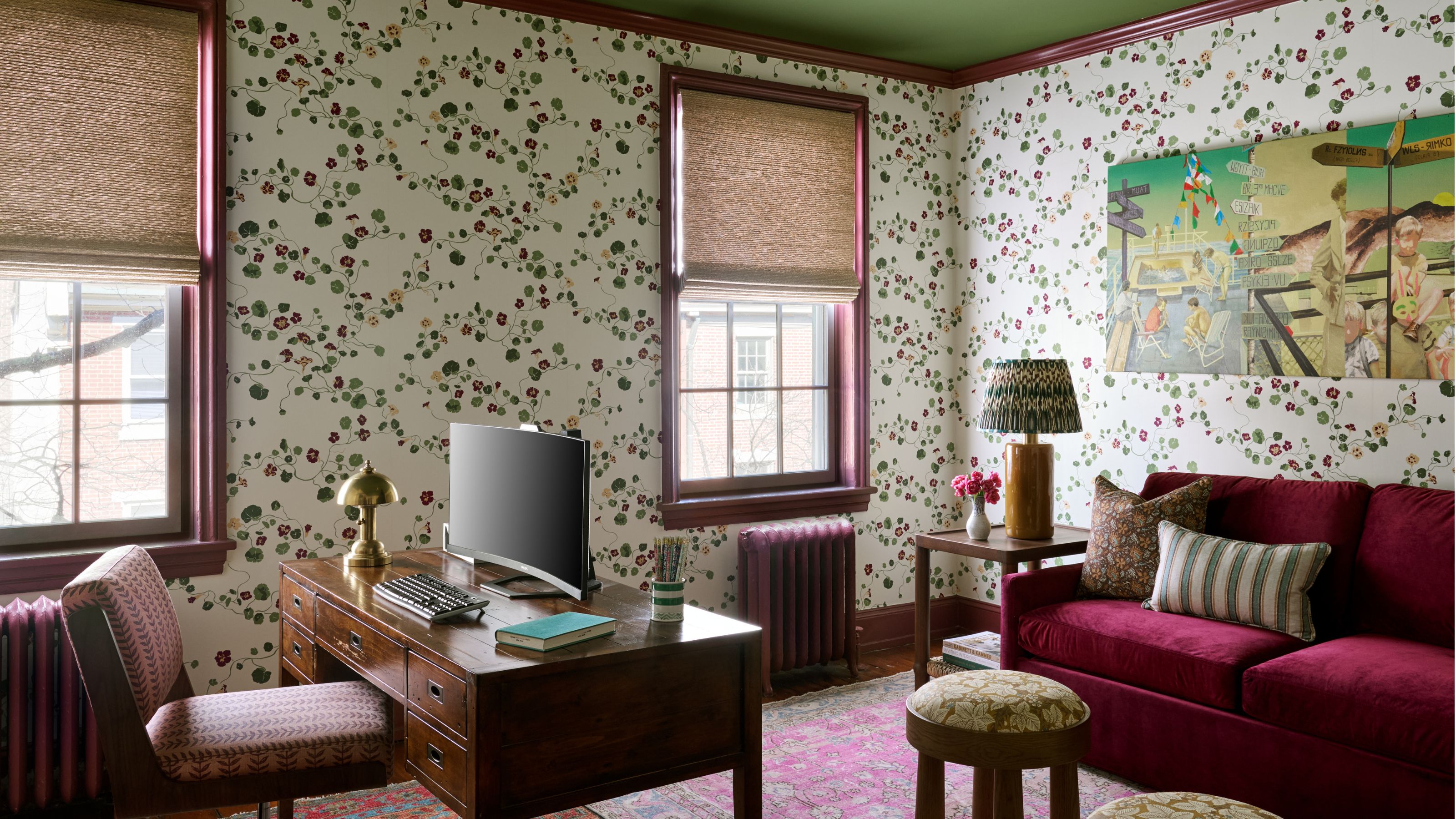 Bureau à domicile avec papier peint à fleurs, plafond vert, bureau en bois vintage, canapé en velours bordeaux et tapis rose vif.