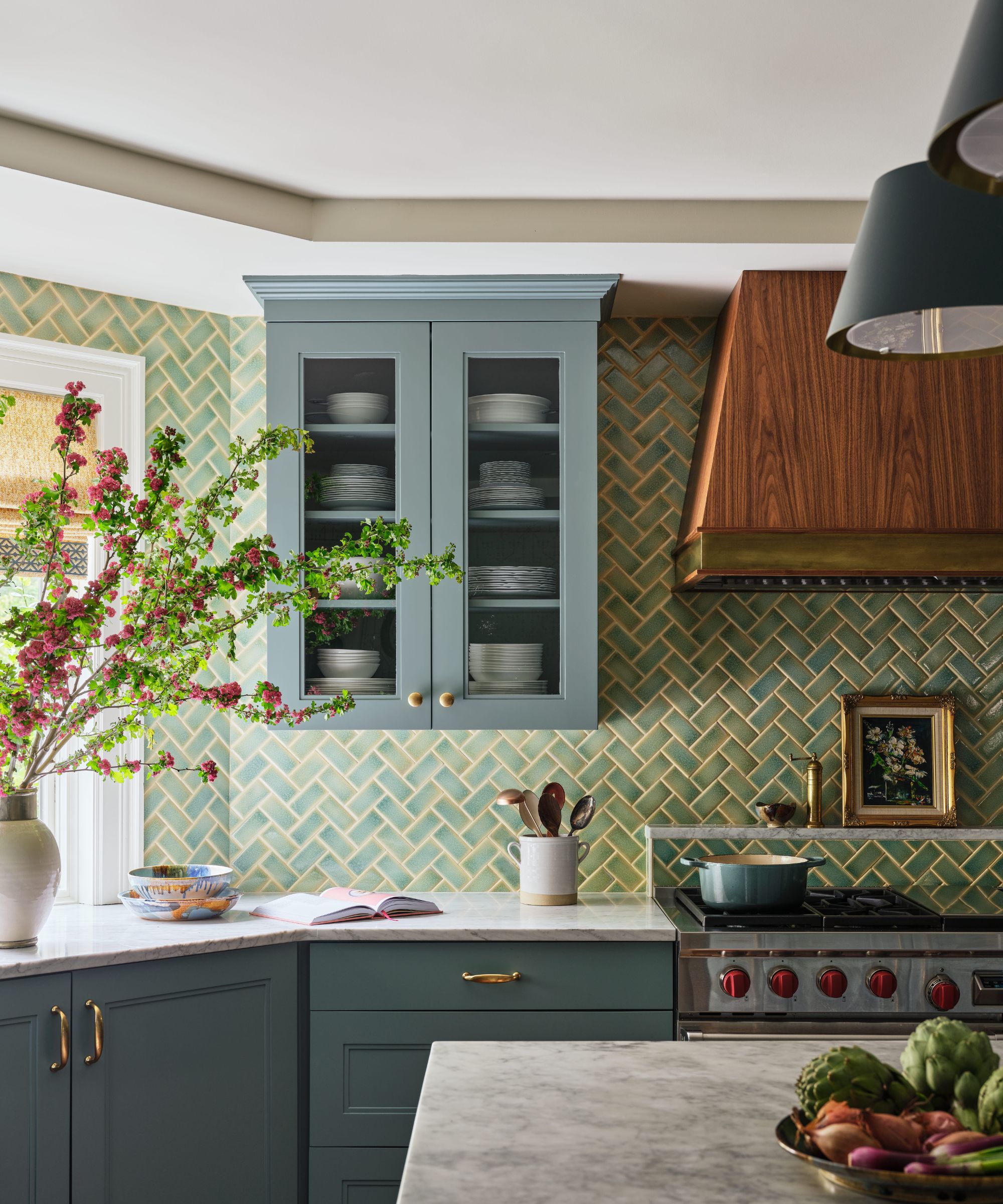 Coin cuisine avec armoires bleu-vert foncé, dosseret en carreaux à chevrons verts et hotte en bois au-dessus de la cuisinière.