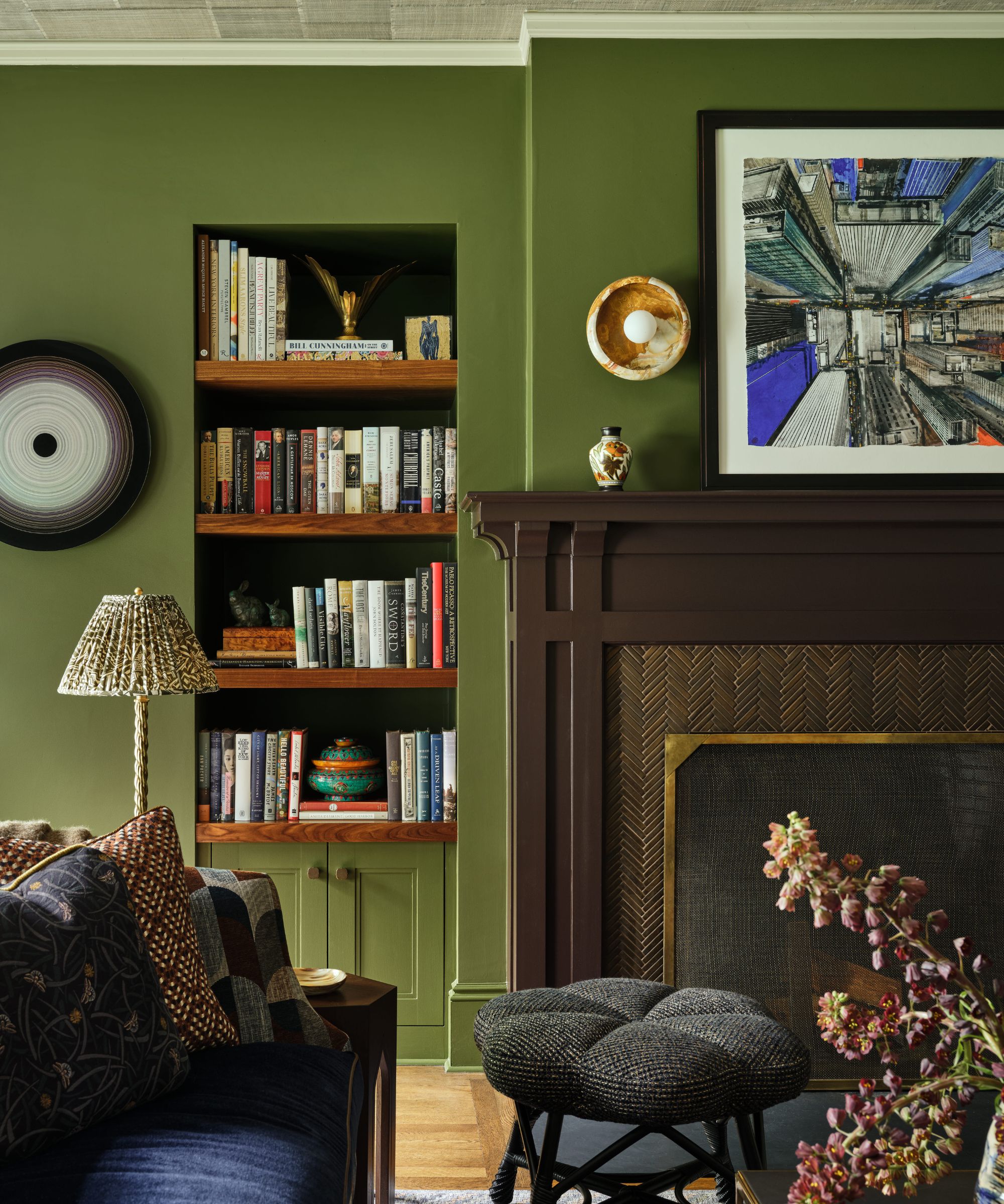 Mur de salon vert avec manteau de cheminée marron foncé, bibliothèque intégrée et œuvres d'art architecturales encadrées.