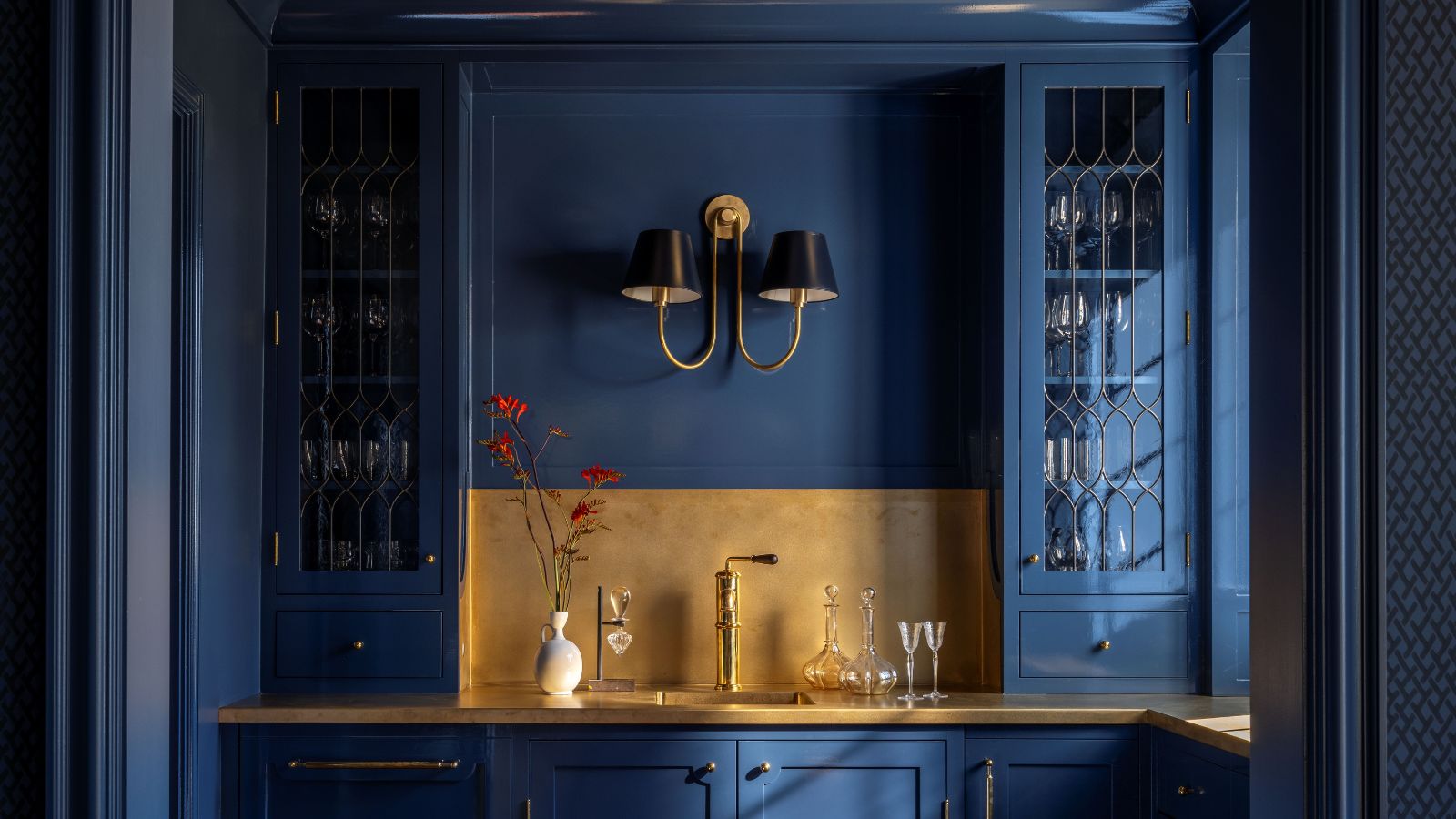 Bar à la maison peint en bleu foncé avec armoires en verre intégrées, dosseret et comptoirs dorés et une grande applique au centre 