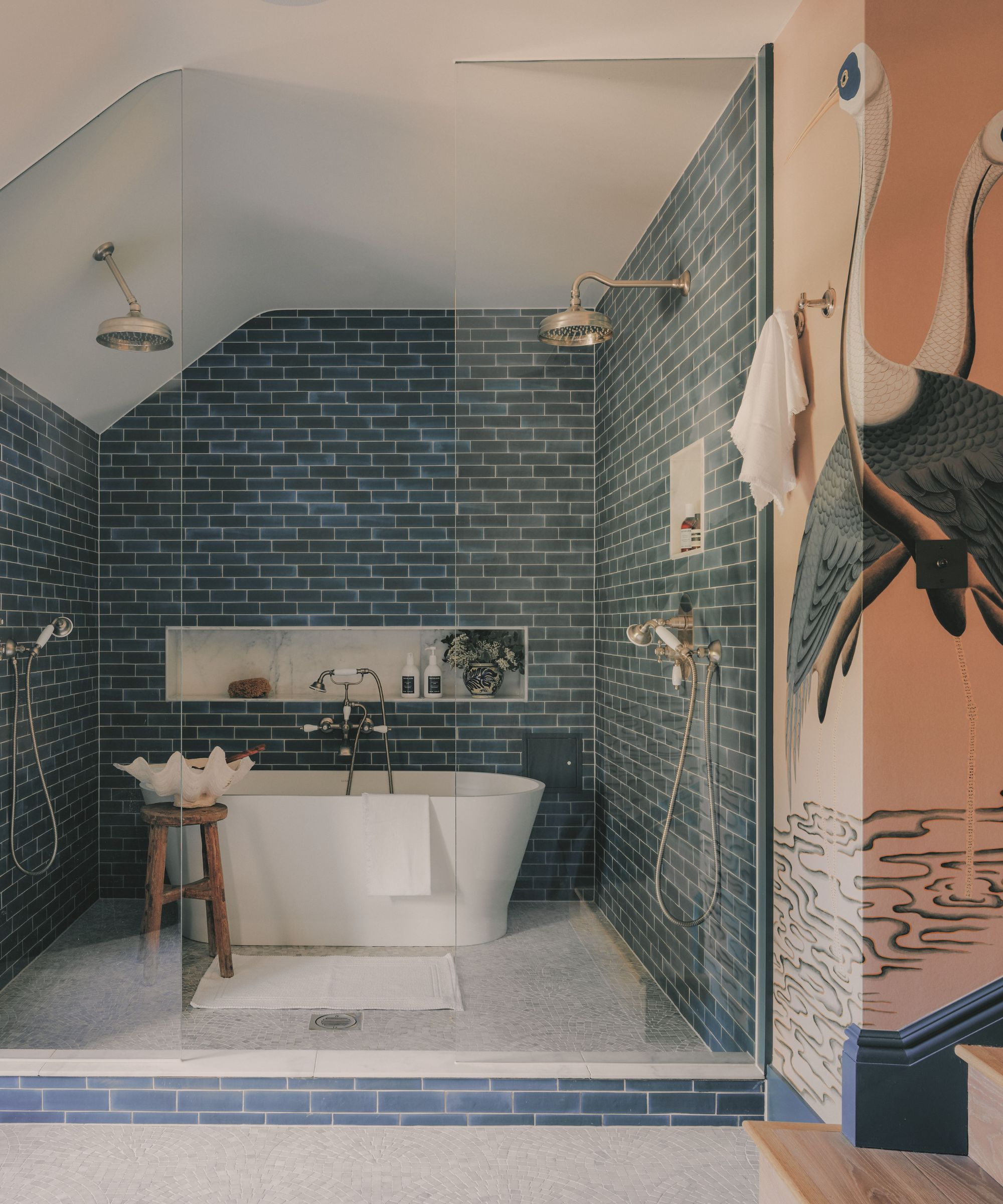 Salle de douche à l'italienne avec carrelage métro bleu foncé, double pomme de douche, baignoire blanche autoportante et mur orné d'une grande fresque murale en forme de héron.