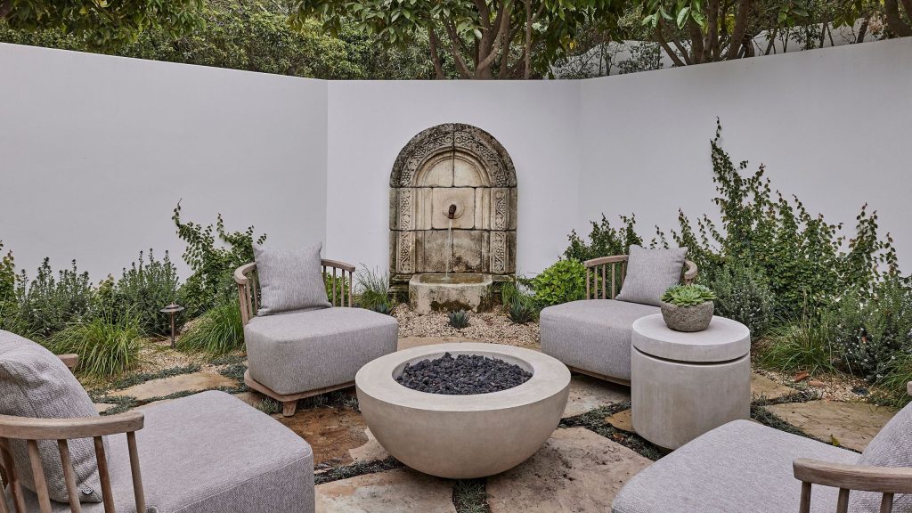 Déplacez-vous sur les canapés, les foyers sculpturaux deviennent le point central de chaque arrière-cour élégante – Achetez 16 des plus chics a walled spanish-style courtyard garden seating area with a stone water feature, stone flooring and firepit at the center