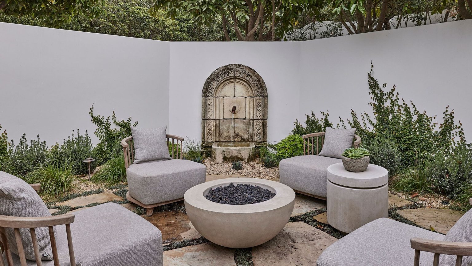 Déplacez-vous sur les canapés, les foyers sculpturaux deviennent le point central de chaque arrière-cour élégante – Achetez 16 des plus chics a walled spanish-style courtyard garden seating area with a stone water feature, stone flooring and firepit at the center