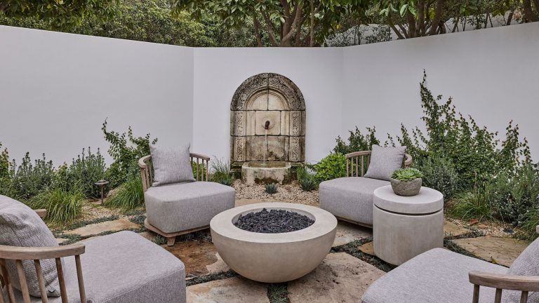 a walled spanish-style courtyard garden seating area with a stone water feature, stone flooring and firepit at the center