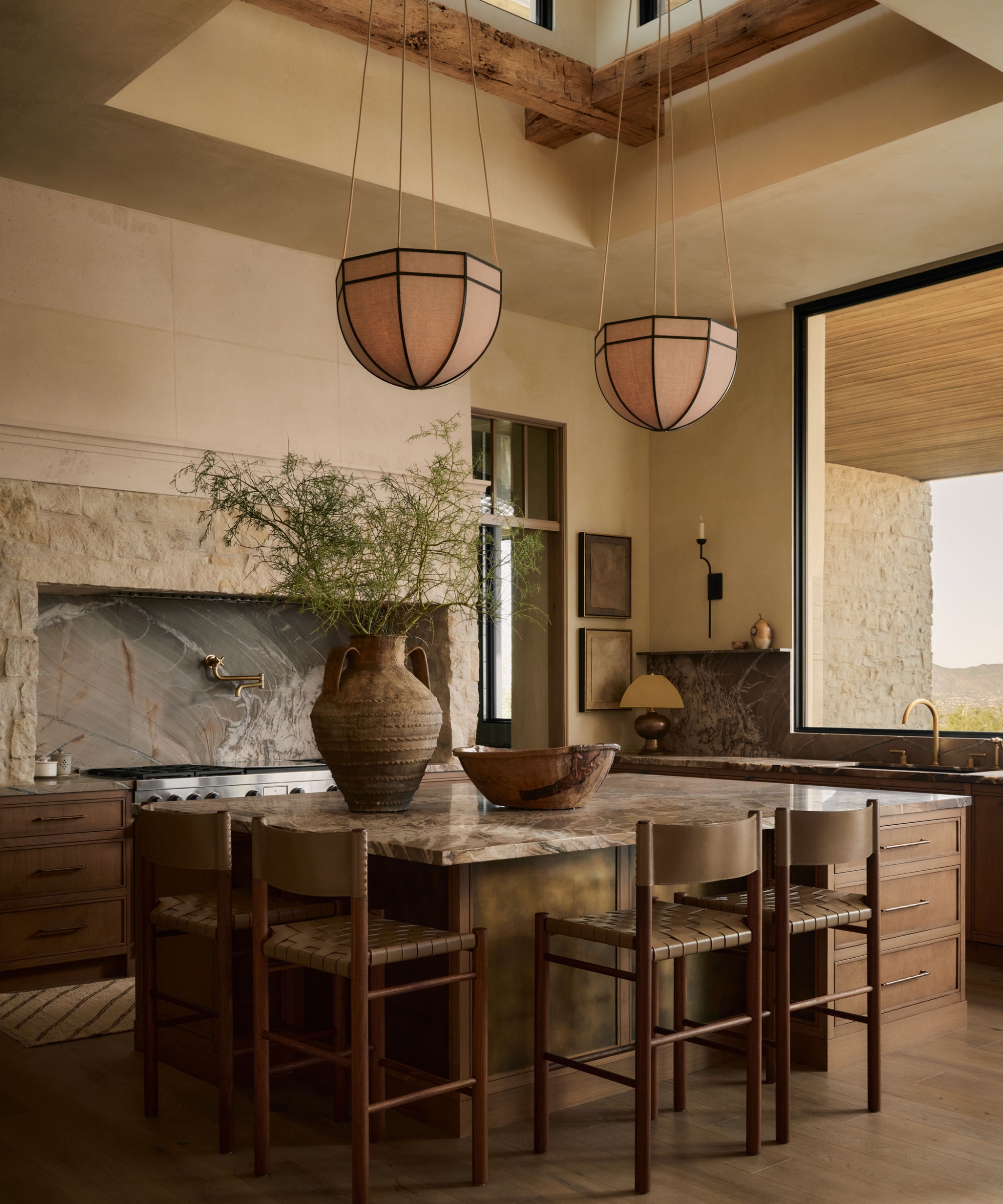 Une cuisine neutre et chaleureuse avec un îlot en bois, des comptoirs en pierre, un plafond voûté avec un puits de lumière et une grande fenêtre au-dessus de l'évier pour maximiser la vue panoramique sur l'Arizona.