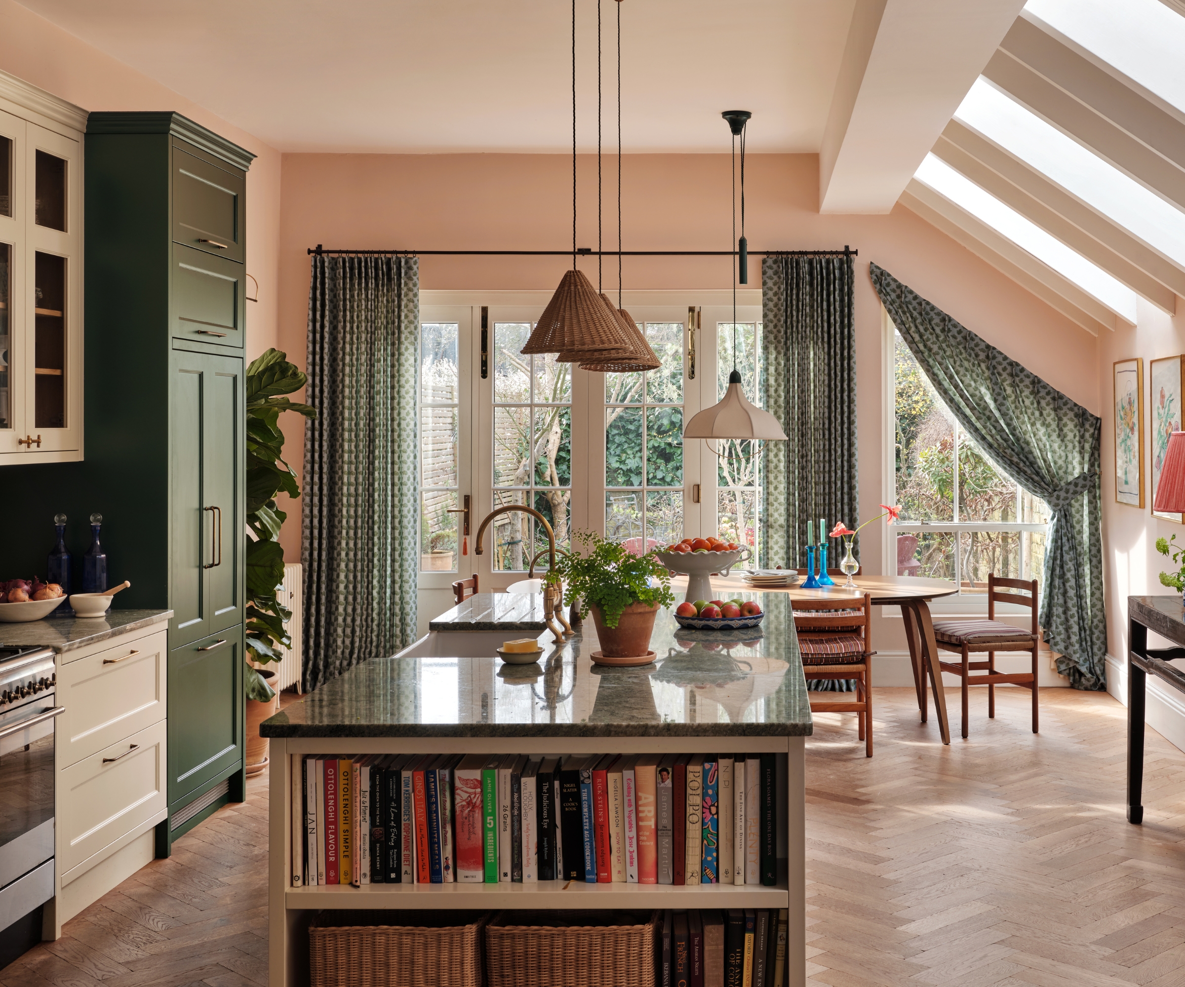 Une cuisine ouverte avec des comptoirs verts, des armoires blanches et vertes, du parquet, une table à manger ovale en bois et des rideaux verts
