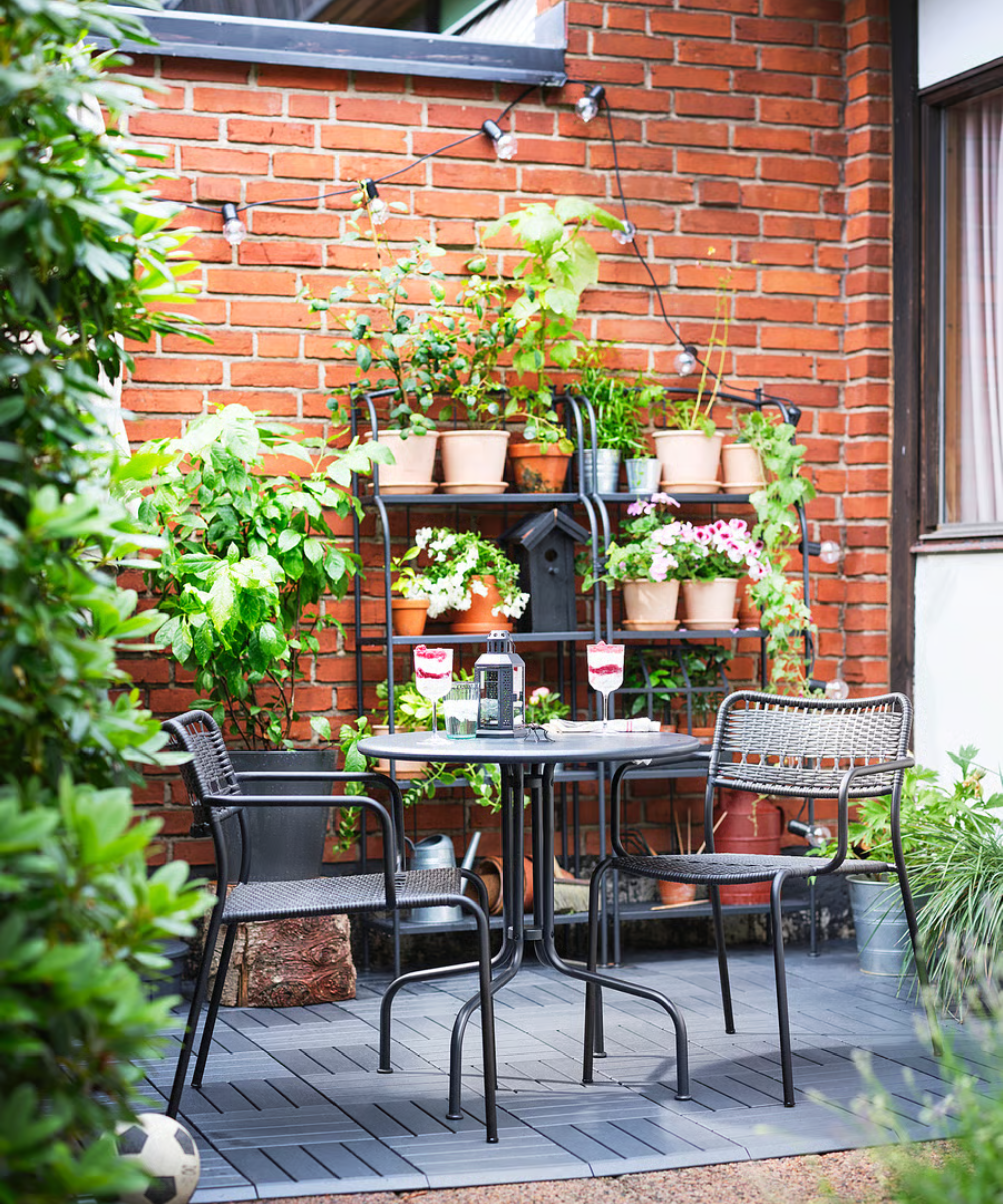 une salle à manger extérieure aménagée avec deux chaises, une table et deux étagères en arrière-plan contenant des plantes