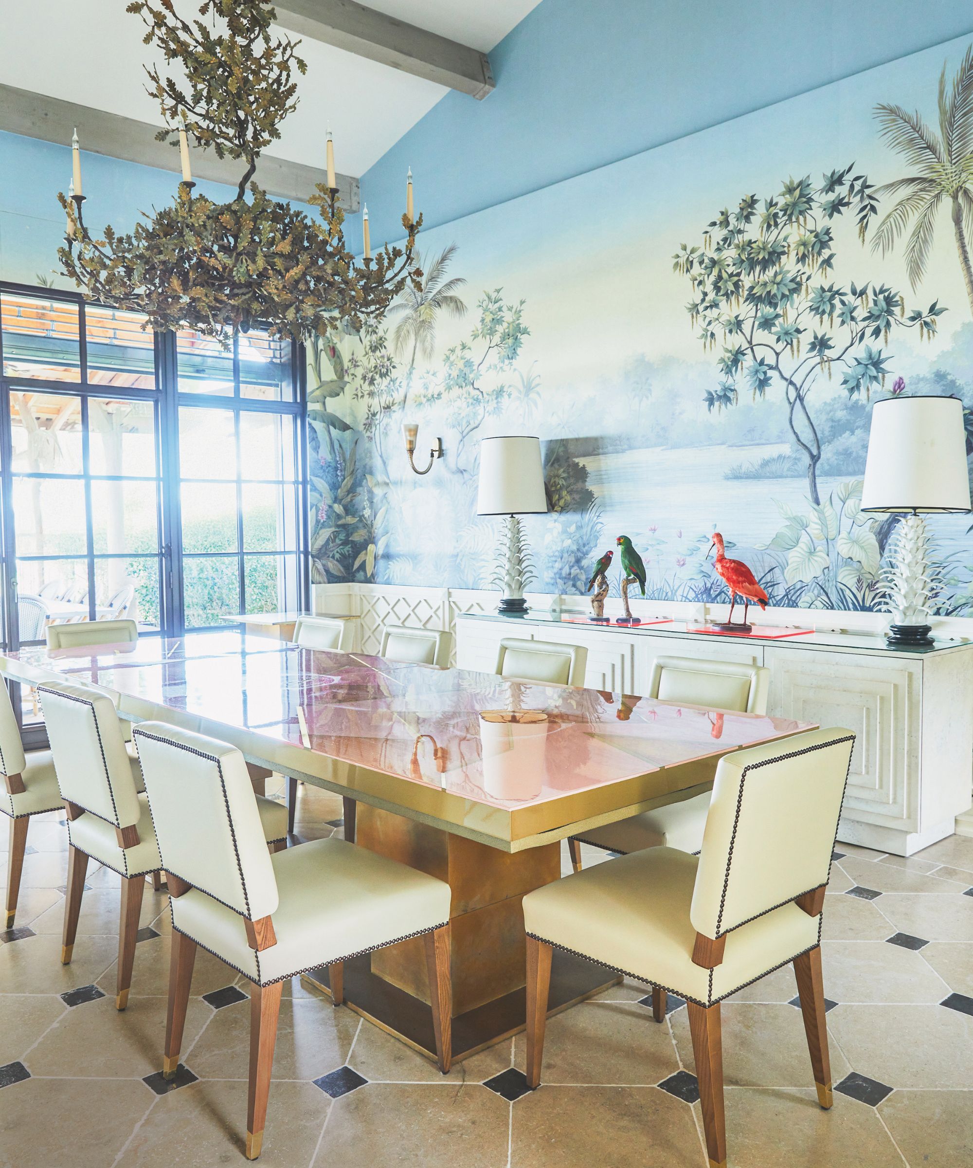 Salle à manger avec une table brillante, des chaises en cuir crème et une fresque murale tropicale au mur